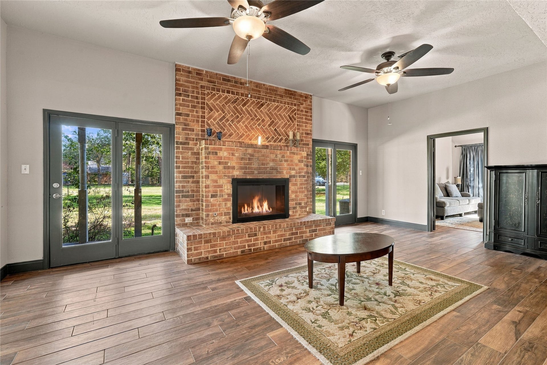 24904 Robin Hood Lane, Hockley, TX 77447 Spacious living room featuring a striking brick fireplace, dual ceiling fans, and glass doors providing views of the surrounding property.