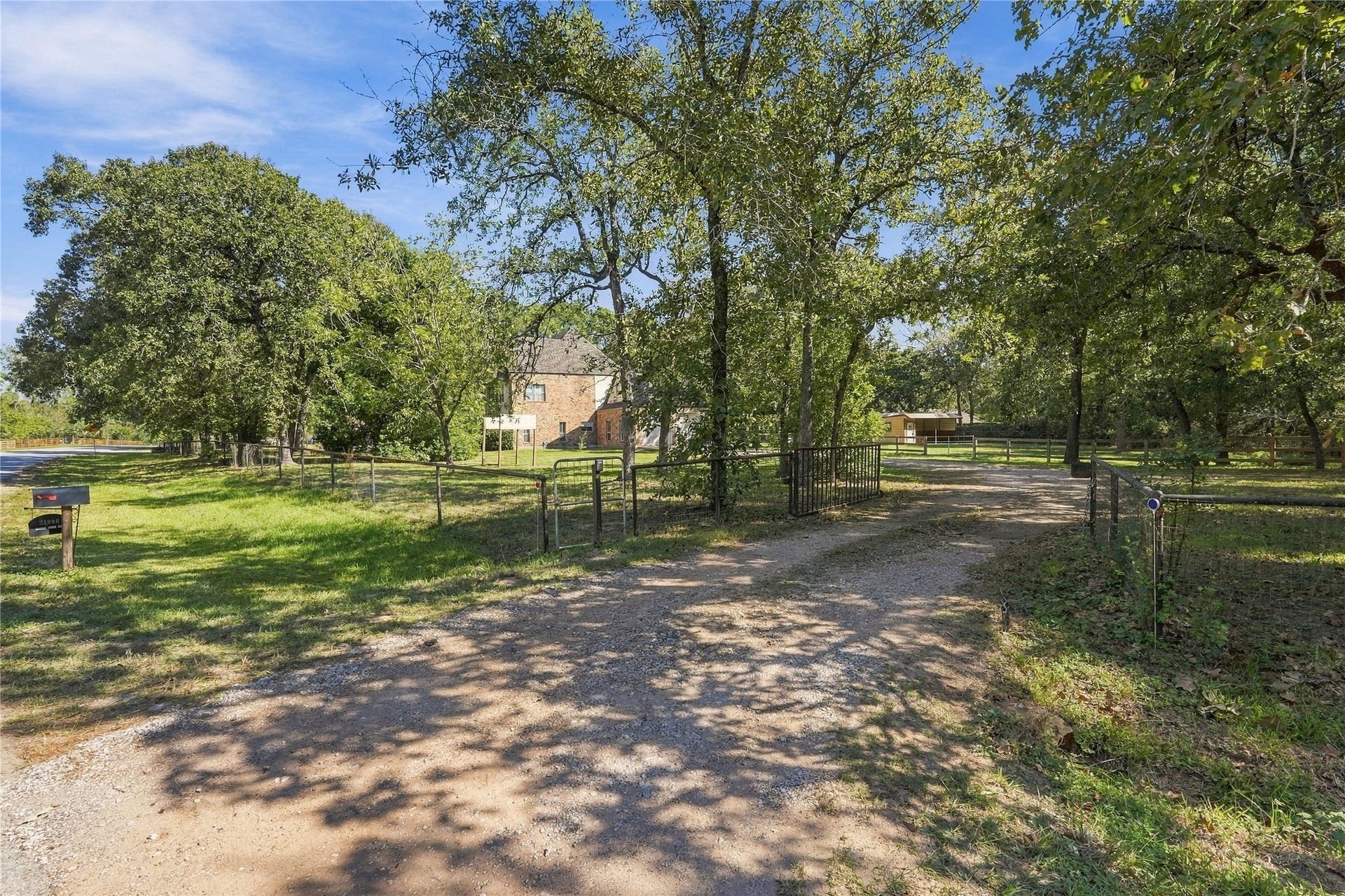 24904 Robin Hood Lane, Hockley, TX 77447 Gated property entrance with a gravel driveway surrounded by mature trees and natural landscaping.
