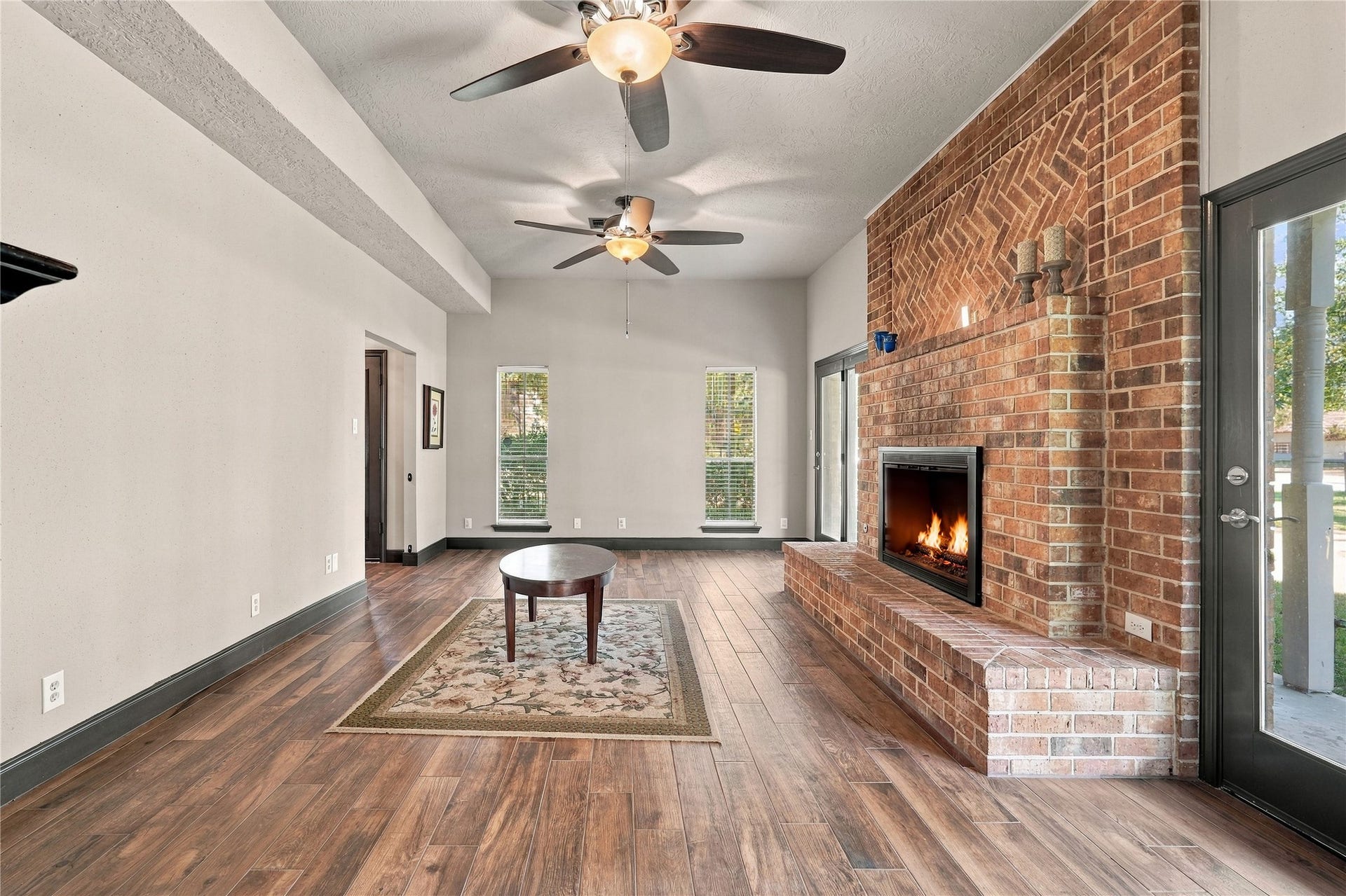 24904 Robin Hood Lane, Hockley, TX 77447 Spacious living room featuring a stunning floor-to-ceiling brick fireplace, wood-look flooring, abundant natural light, and French doors providing access to the covered porch.