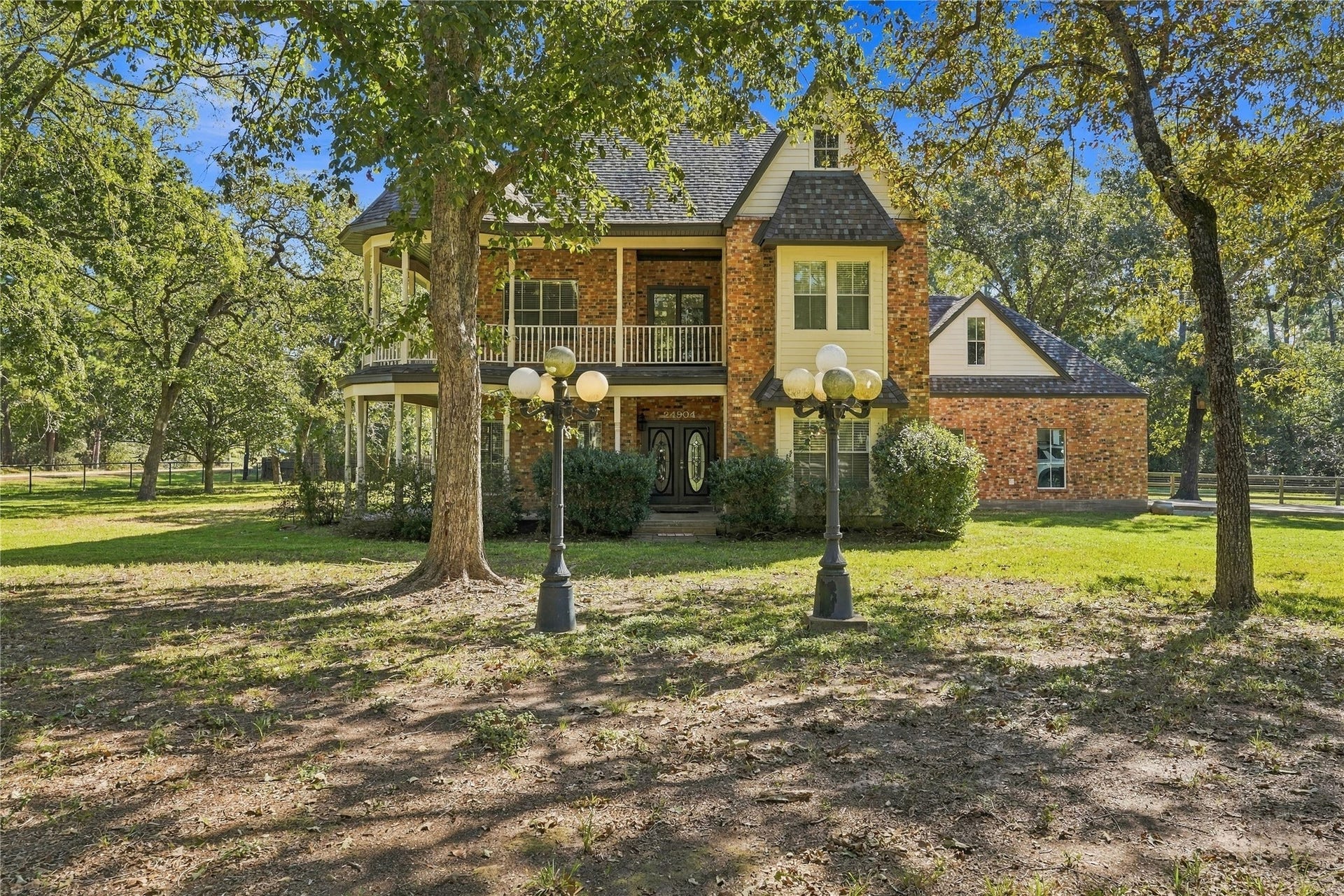 24904 Robin Hood Lane, Hockley, TX 77447 Beautiful two-story brick home surrounded by mature trees, featuring a covered front porch and second-story balcony.