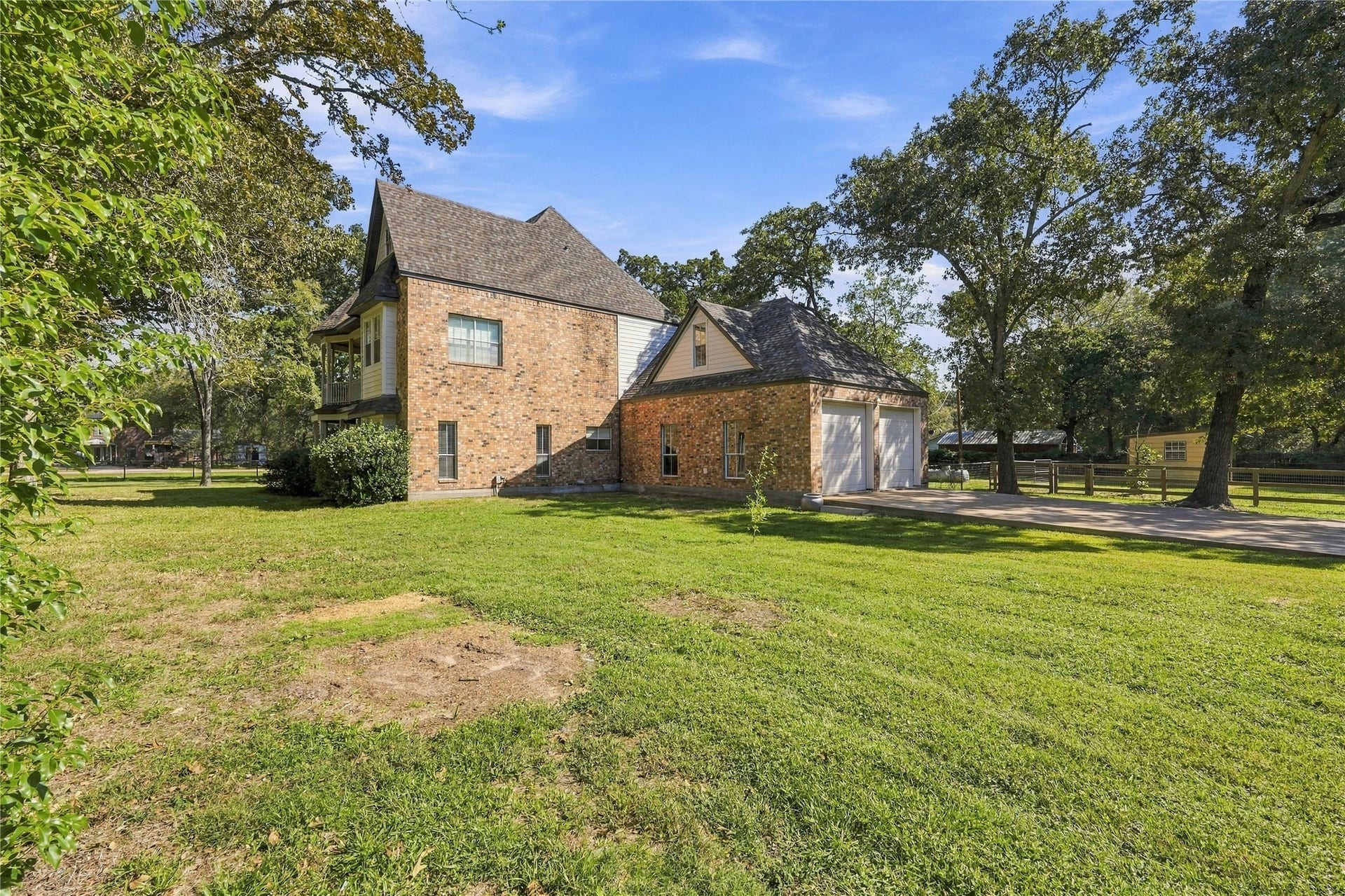 24904 Robin Hood Lane, Hockley, TX 77447 Side exterior showcasing the brick home, attached two-car garage, and spacious lawn surrounded by mature trees.
