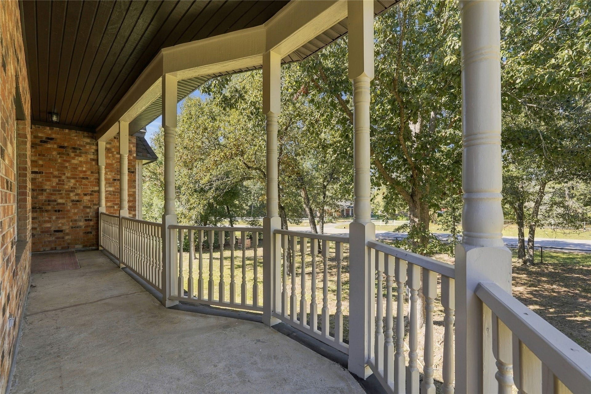 24904 Robin Hood Lane, Hockley, TX 77447 Expansive covered balcony featuring decorative columns, railing, and peaceful views of the mature trees and surrounding property.