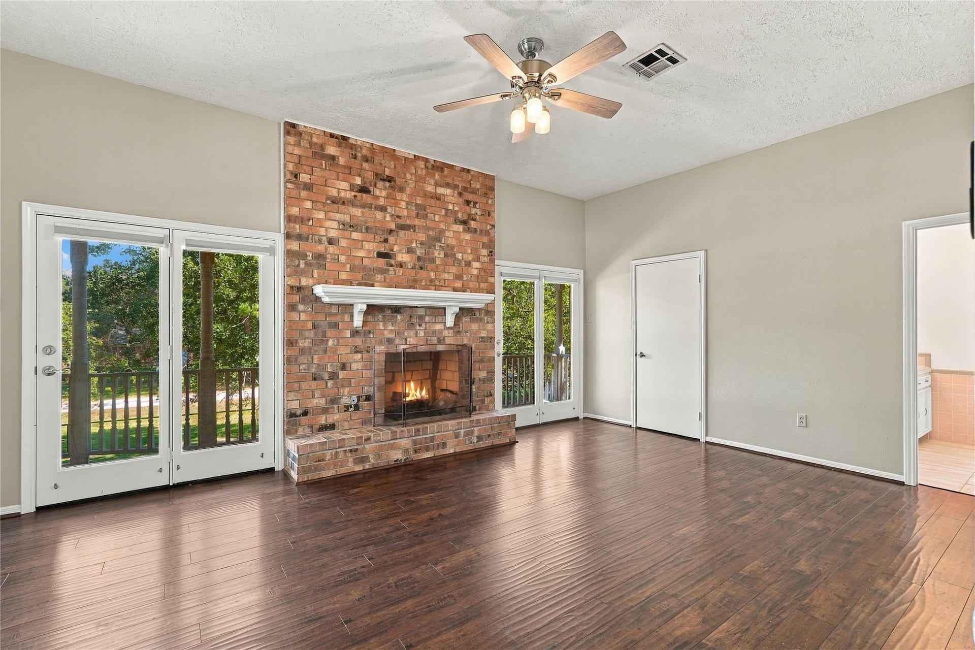 24904 Robin Hood Lane, Hockley, TX 77447 Spacious primary bedroom featuring a floor-to-ceiling brick fireplace, wood flooring, ceiling fan, and French doors opening to the covered balcony.