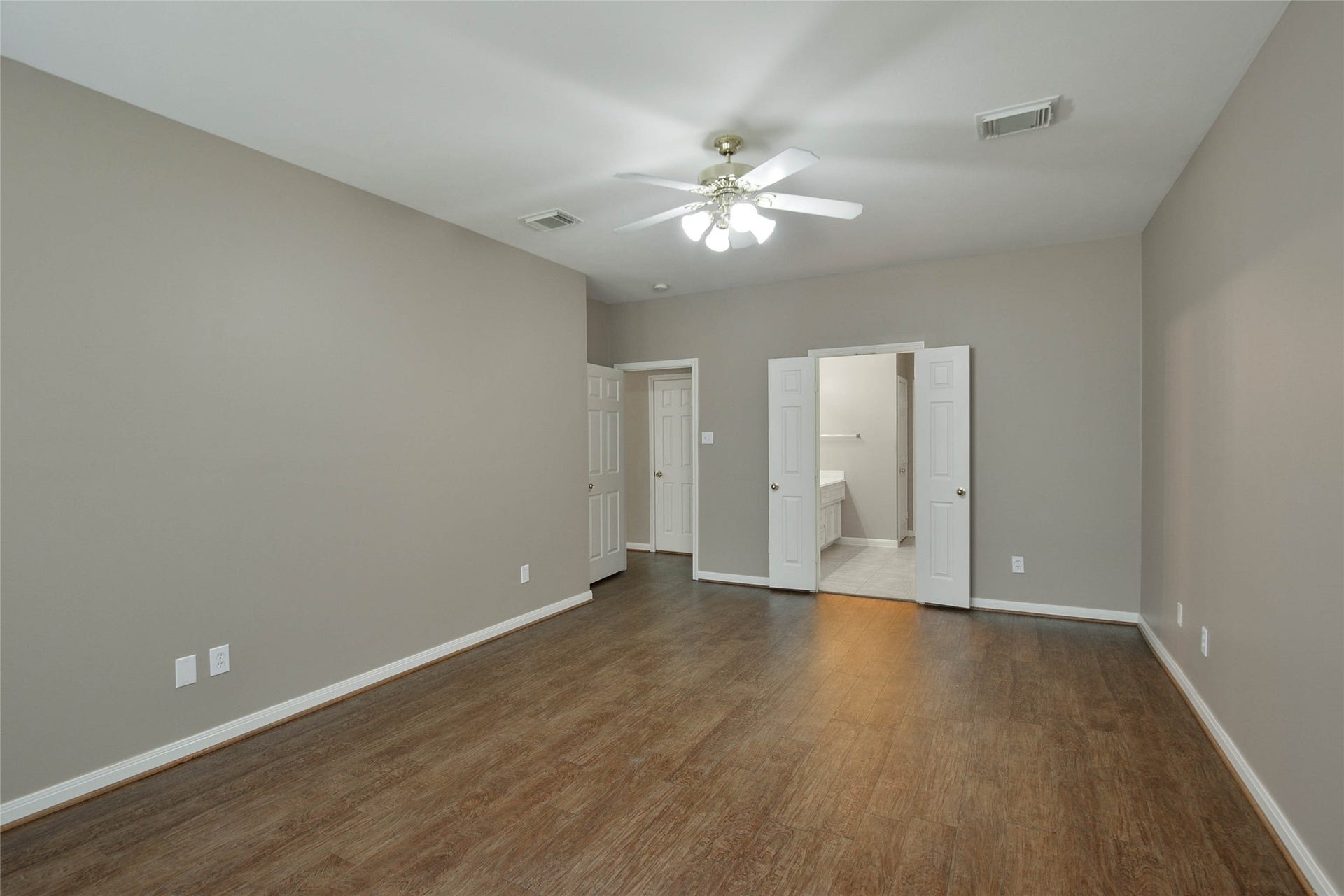 7023 Timber Edge Lane Lane, Humble, TX 77346 Primary bedroom with elegant wood flooring, neutral walls, and a ceiling fan, leading to an en-suite bathroom with double doors.