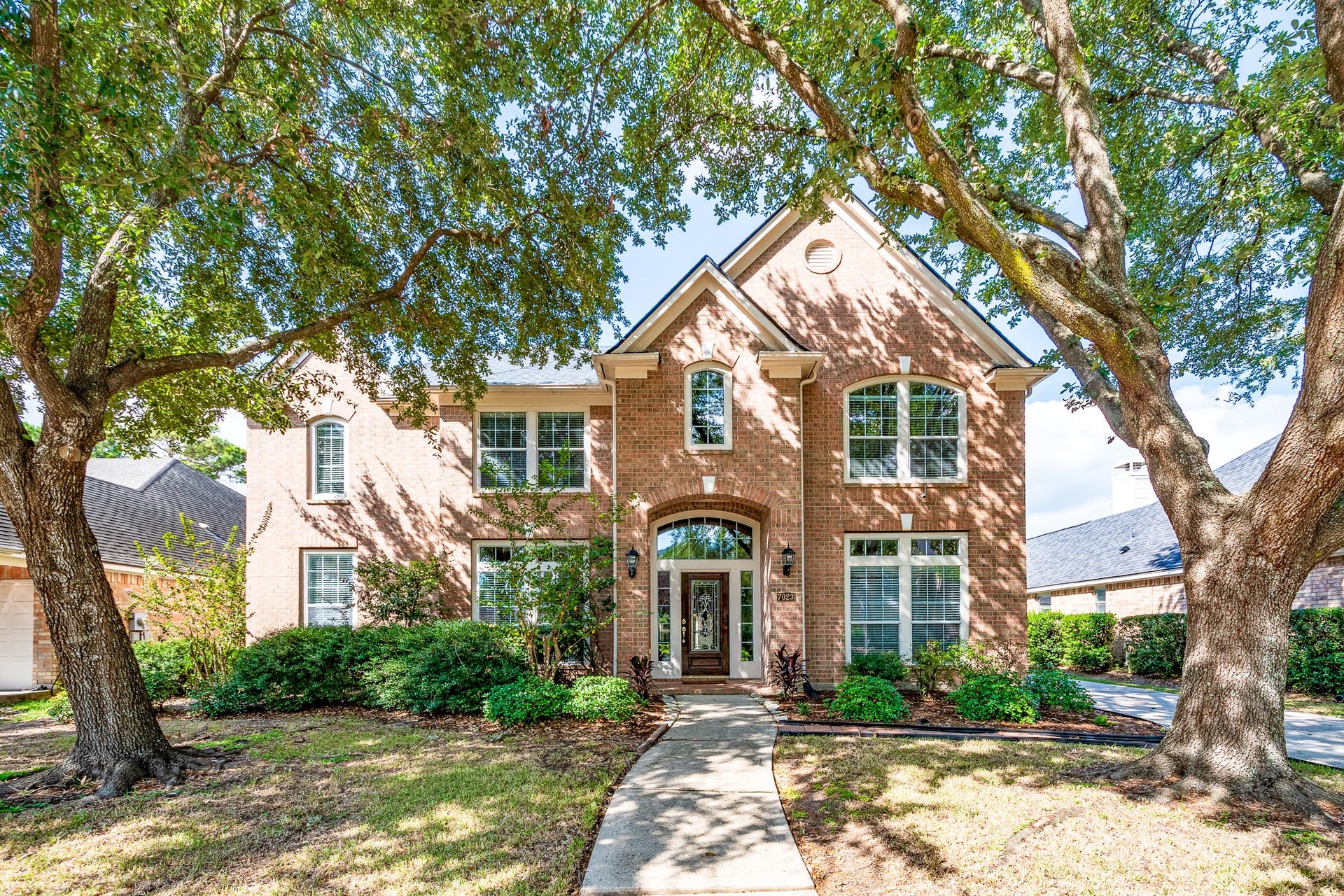 7023 Timber Edge Lane Lane, Humble, TX 77346 Stately two-story brick home with large arched windows, surrounded by mature trees and lush landscaping, offers welcoming curb appeal.