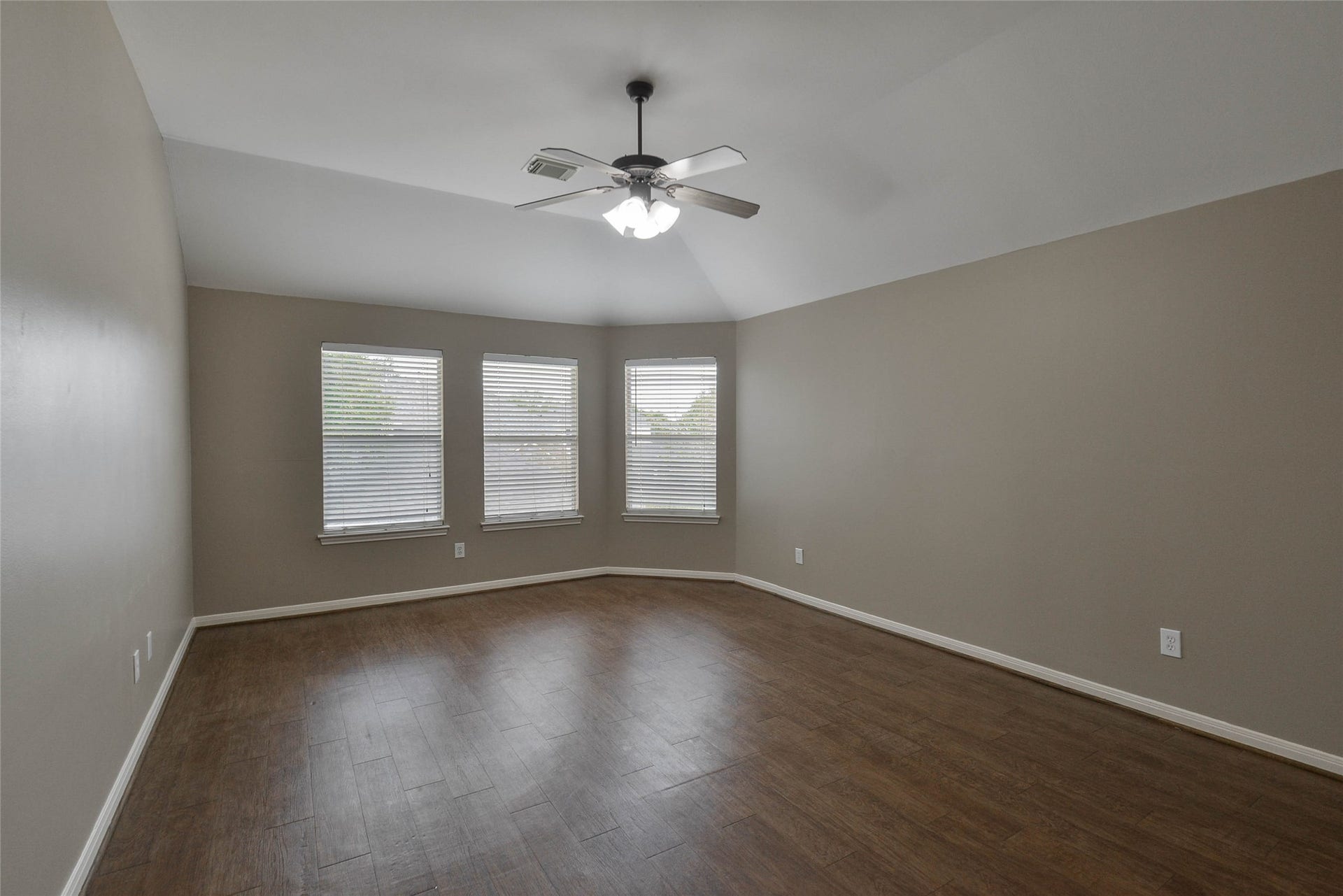 7023 Timber Edge Lane Lane, Humble, TX 77346 Secondary bedroom with rich wood flooring, neutral walls, and ample natural light from three large windows; perfect for a cozy retreat.