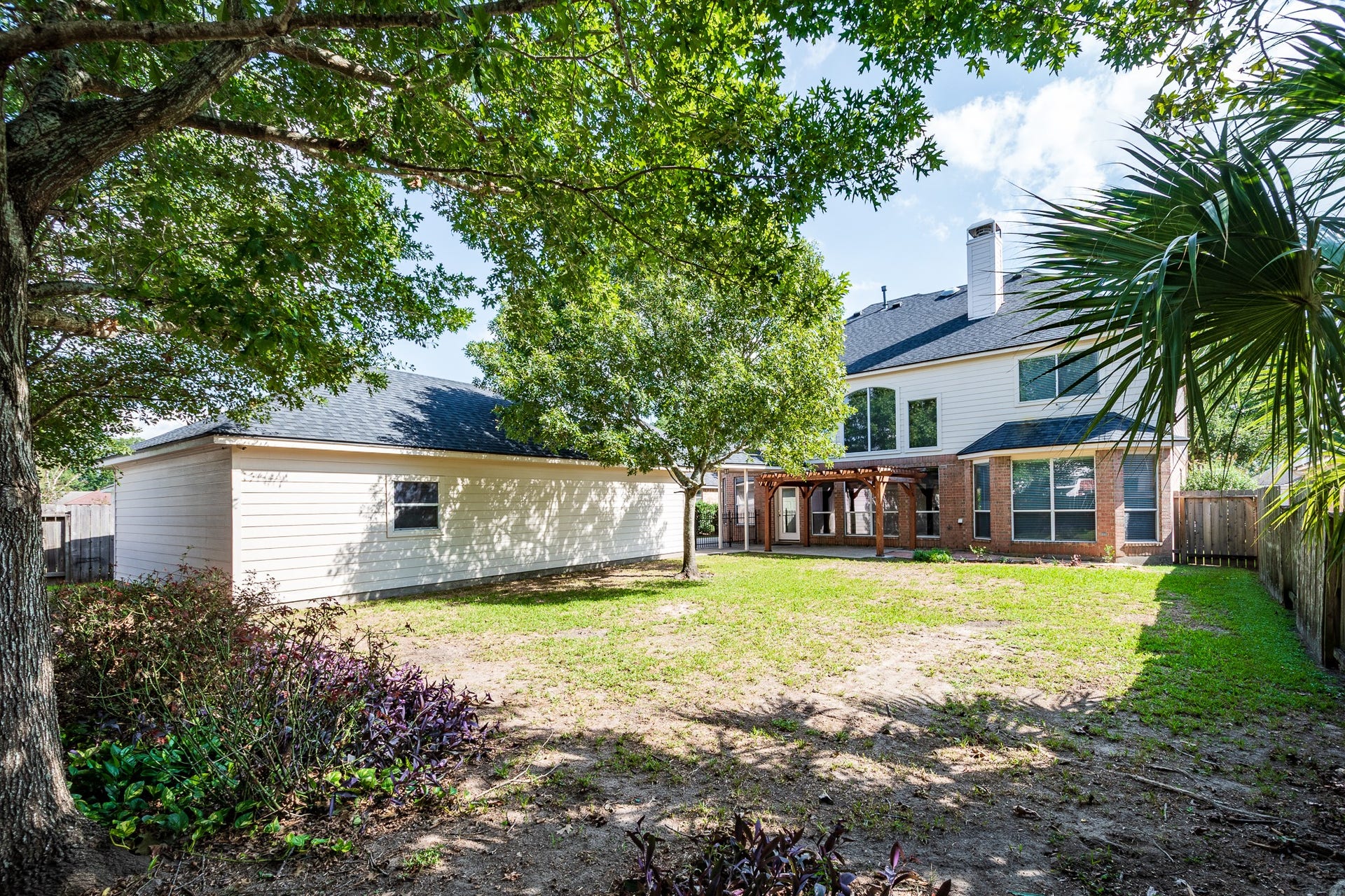 7023 Timber Edge Lane Lane, Humble, TX 77346 Backyard featuring mature trees, a detached garage, and a charming pergola, perfect for outdoor relaxation and entertainment.