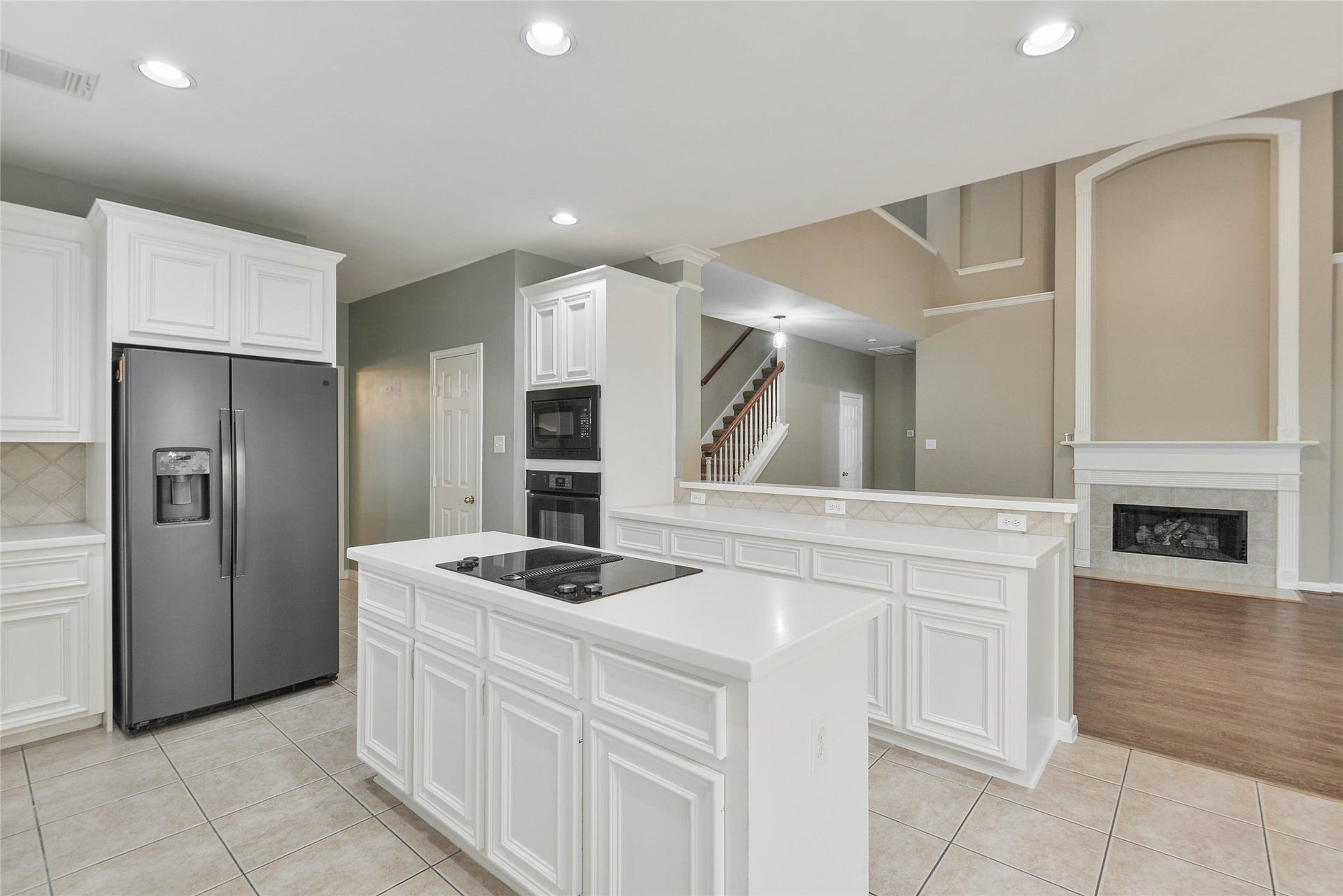 7023 Timber Edge Lane Lane, Humble, TX 77346 Kitchen with modern appliances, an island cooktop, and ample white cabinetry, seamlessly flowing into an inviting living area featuring a cozy fireplace and high ceilings.