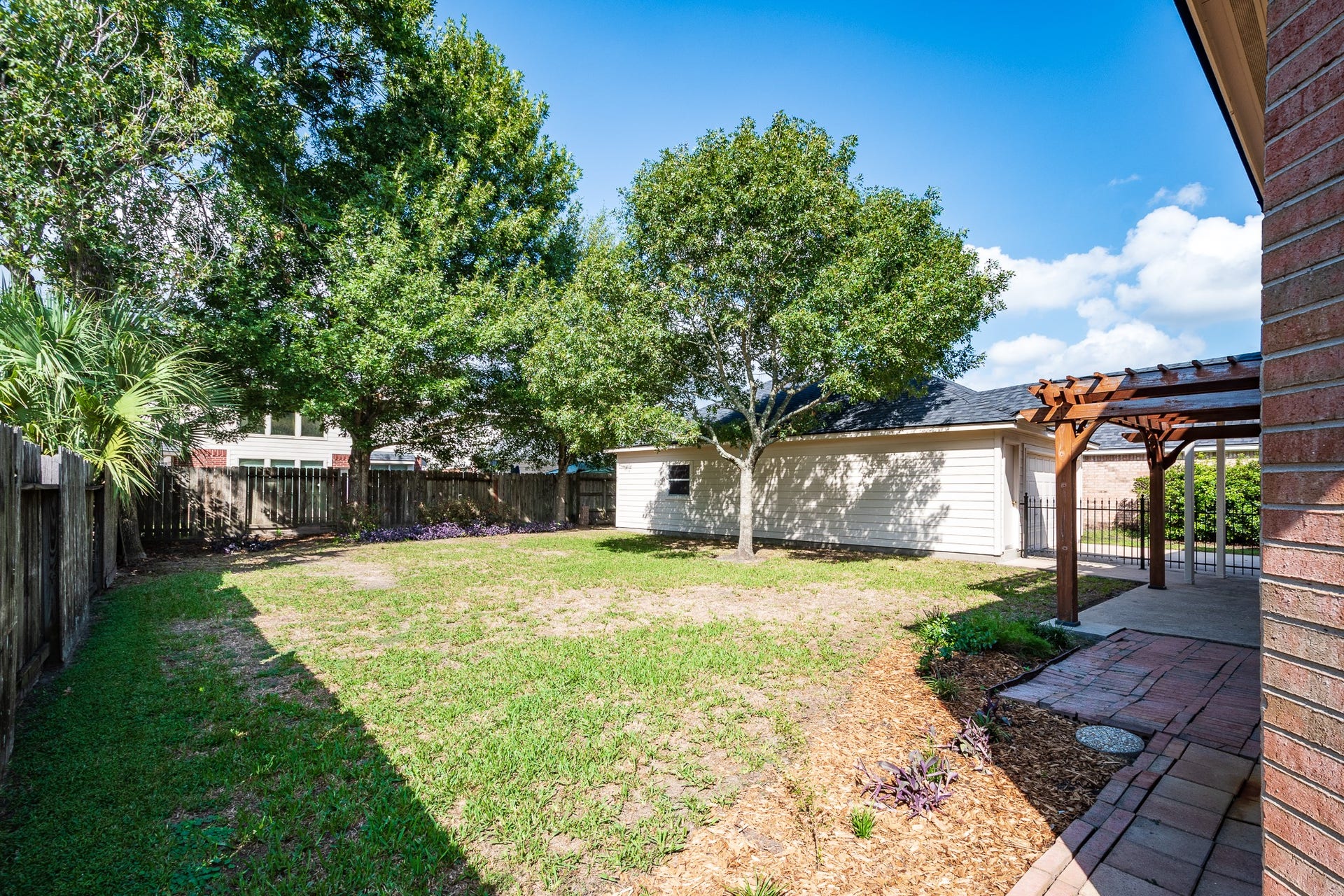 7023 Timber Edge Lane Lane, Humble, TX 77346 Backyard with lush greenery, mature trees, and a charming pergola, perfect for outdoor relaxation and entertaining.