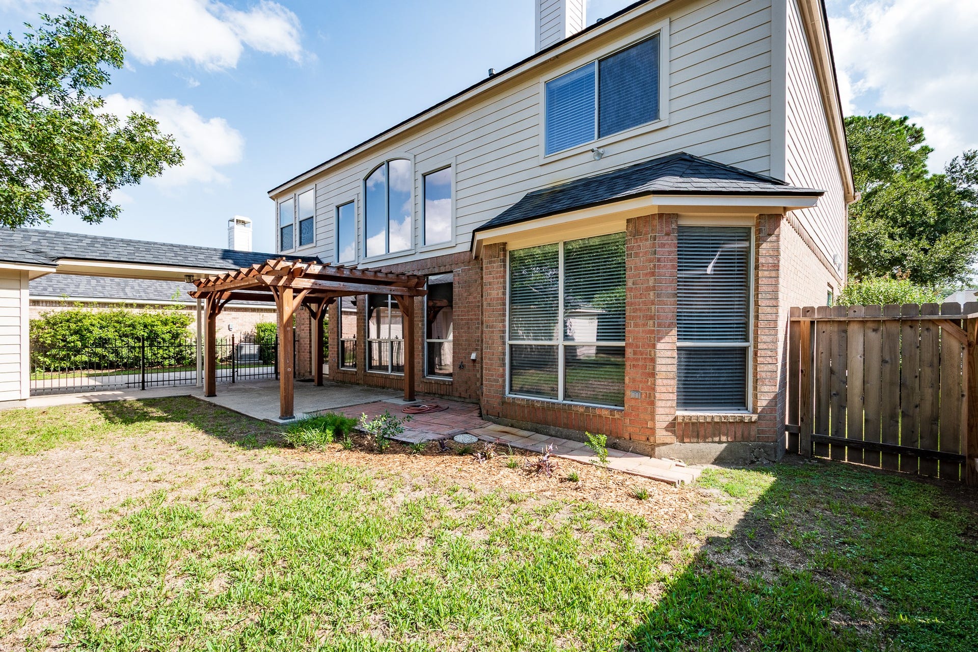 7023 Timber Edge Lane Lane, Humble, TX 77346 Backyard features a charming pergola over a patio, perfect for outdoor relaxation, with large windows offering abundant natural light and a mix of brick and siding for a classic look.