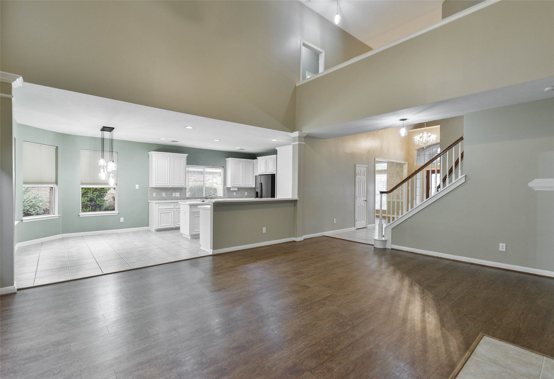 7023 Timber Edge Lane Lane, Humble, TX 77346 Open-concept living area with elegant wood flooring, transitioning seamlessly into a modern kitchen with sleek white cabinetry and large windows for ample natural light.