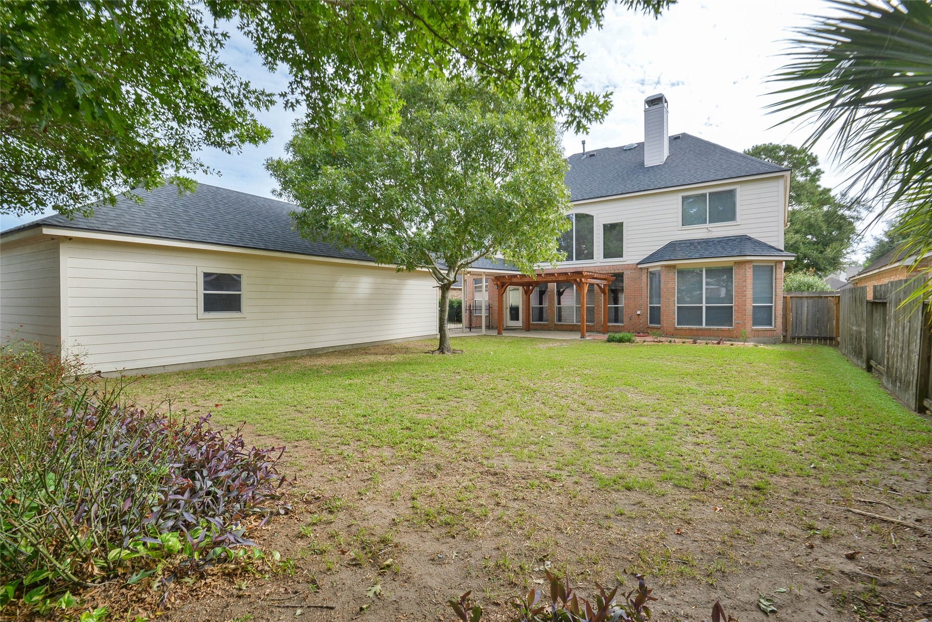 7023 Timber Edge Lane Lane, Humble, TX 77346 Backyard featuring lush greenery, a charming pergola, and a large two-story home with a detached garage, perfect for outdoor relaxation and entertaining.