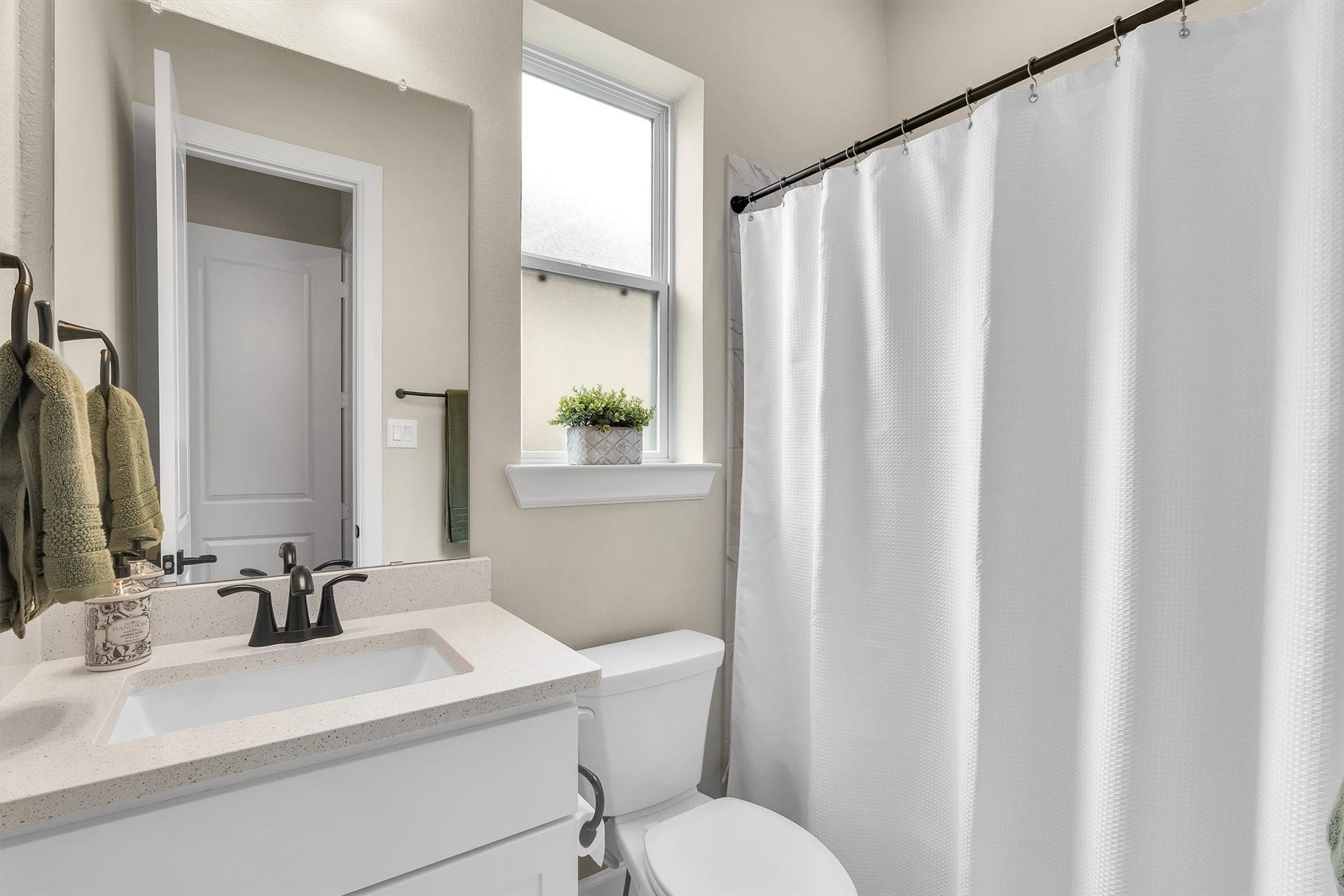 Modern bathroom featuring a sleek white vanity, a large mirror, and a tub with a white shower curtain. Plenty of natural light