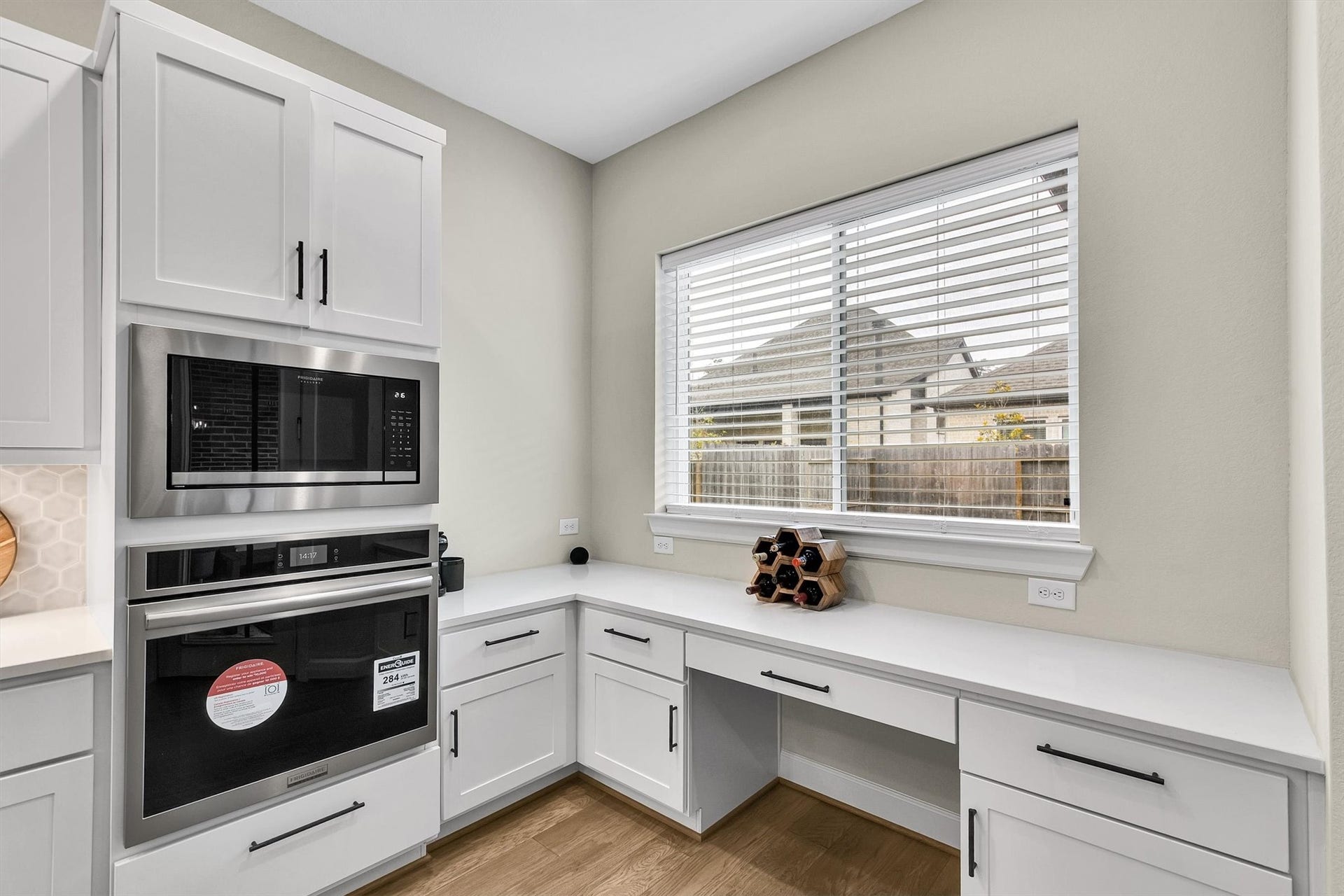 Built-in stainless steel microwave and oven, and a spacious countertop beneath a large window with blinds, offering plenty of natural light.