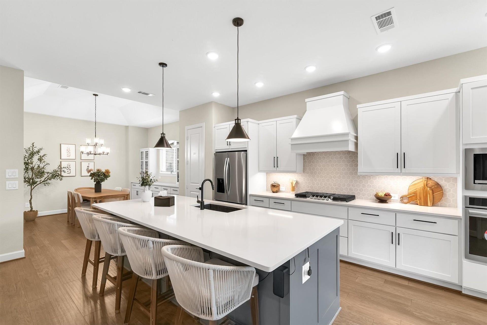 This modern kitchen features a spacious open layout with a large island, sleek white cabinetry, stainless steel appliances, and elegant pendant lighting. The adjacent dining area is bright and inviting, perfect for entertaining.
