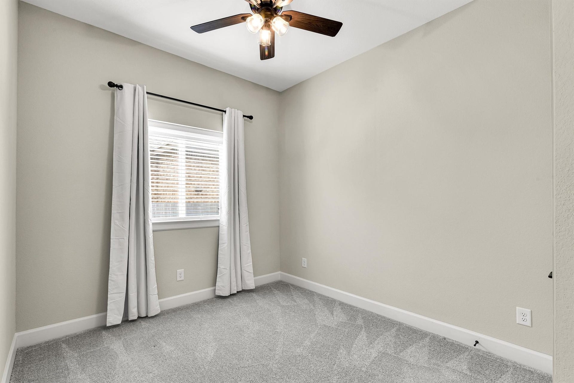 2nd secondary bedroom with its ceiling fan and lights, large window with white curtains, providing natural light. It has gray carpeting, creating a cozy atmosphere.