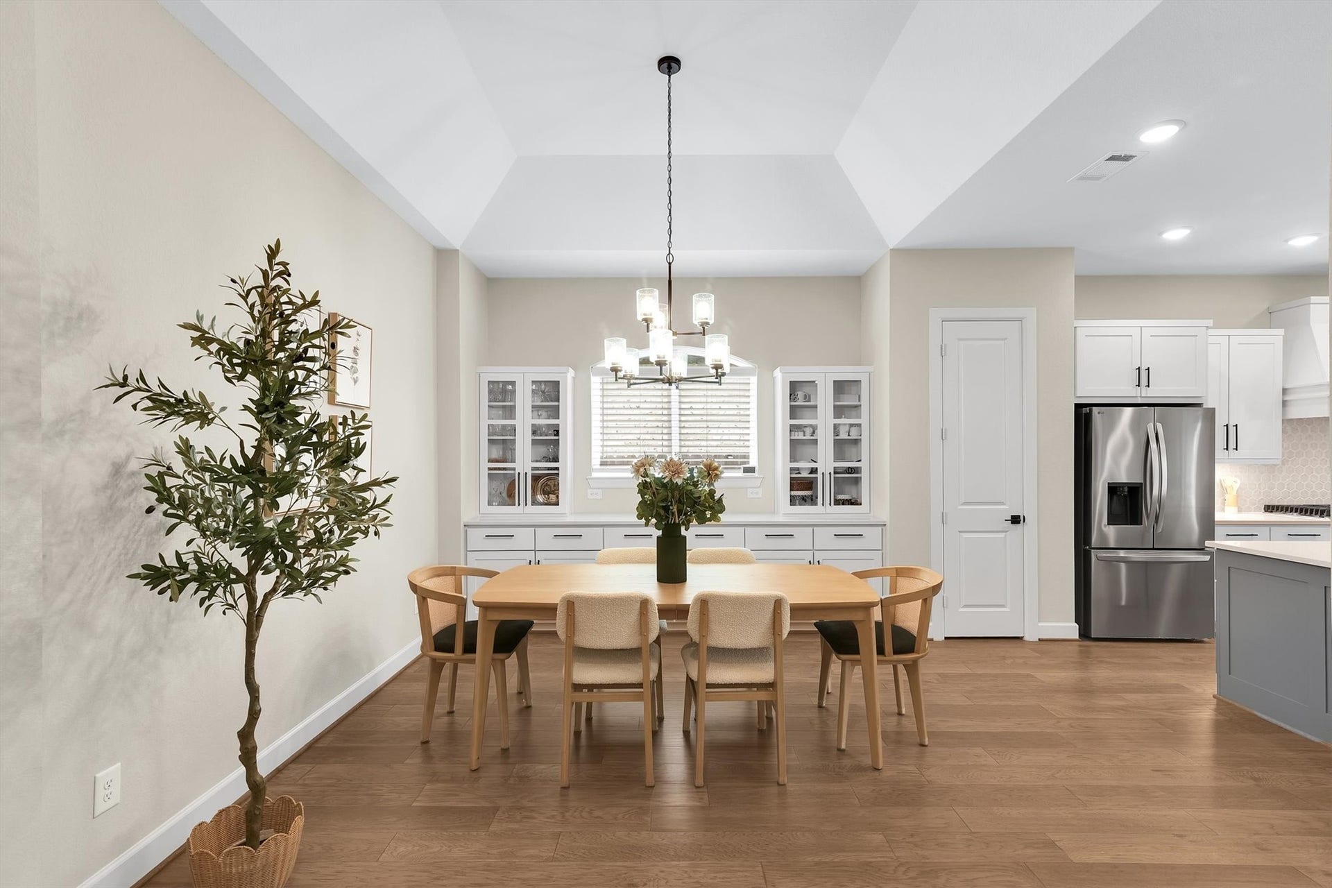 Modern dining area complemented by a stylish chandelier. Built-in cabinetry, neutral walls, and hardwood floors, creating a warm and inviting atmosphere adjacent to a contemporary kitchen.