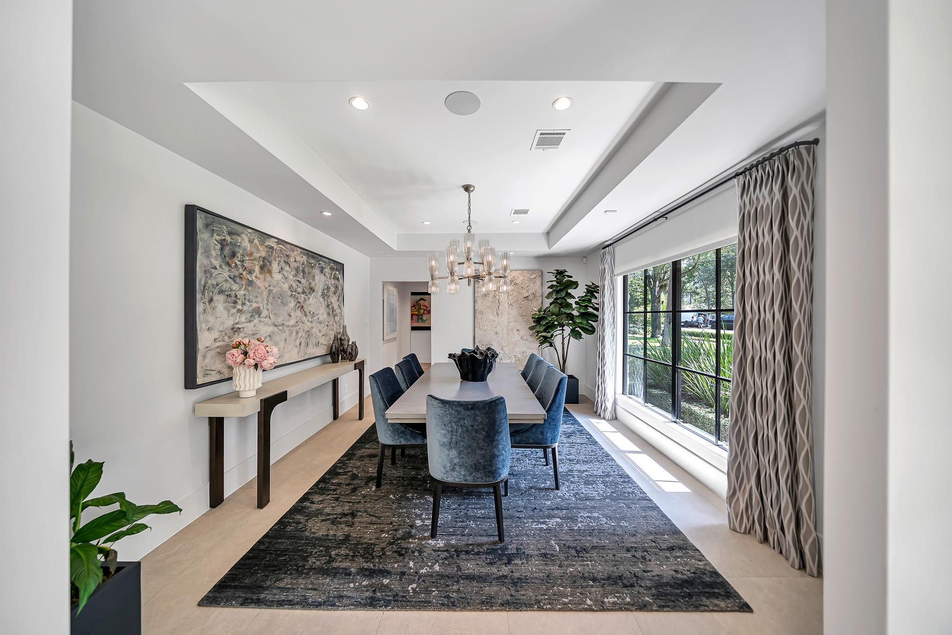Chic formal dining featuring tray ceiling details, recessed lighting, and a modern chandelier. Large picture window offers abundance of natural light.