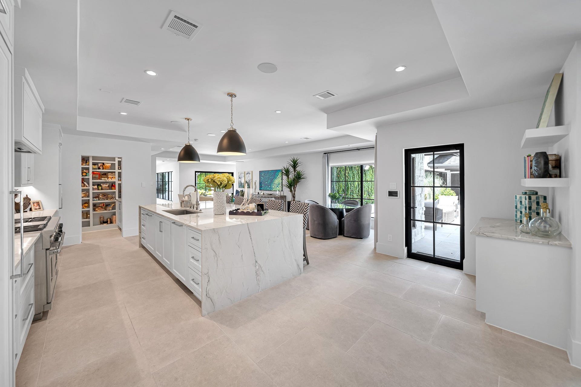 Sleek and modern kitchen with a spacious island, Quartzite countertops, and ample cabinetry, seamlessly flowing into a bright living area with large windows and open access to the patio.