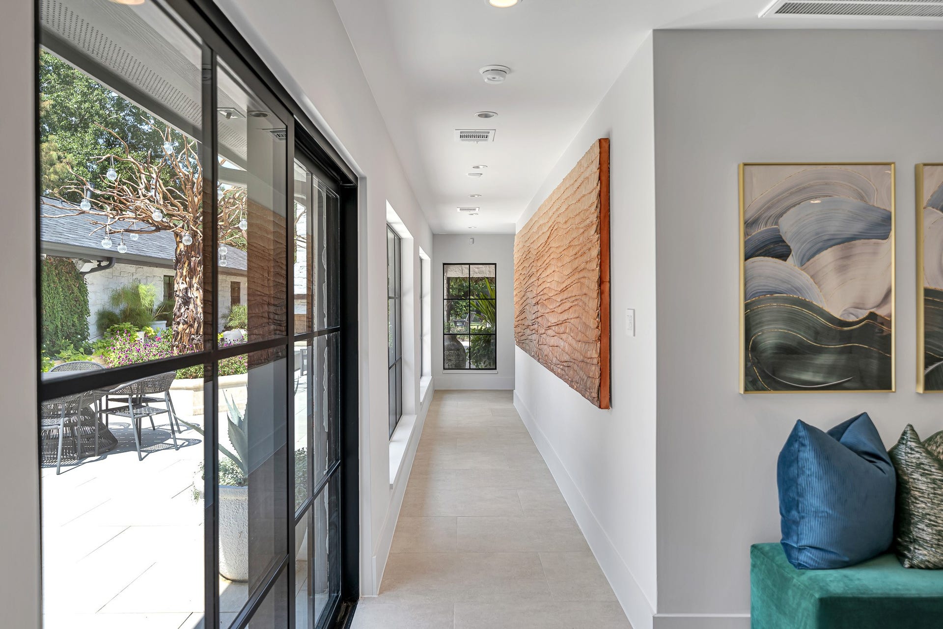 Bright hallway with floor-to-ceiling windows overlooking a serene patio, with space to feature elegant artwork and modern accents.