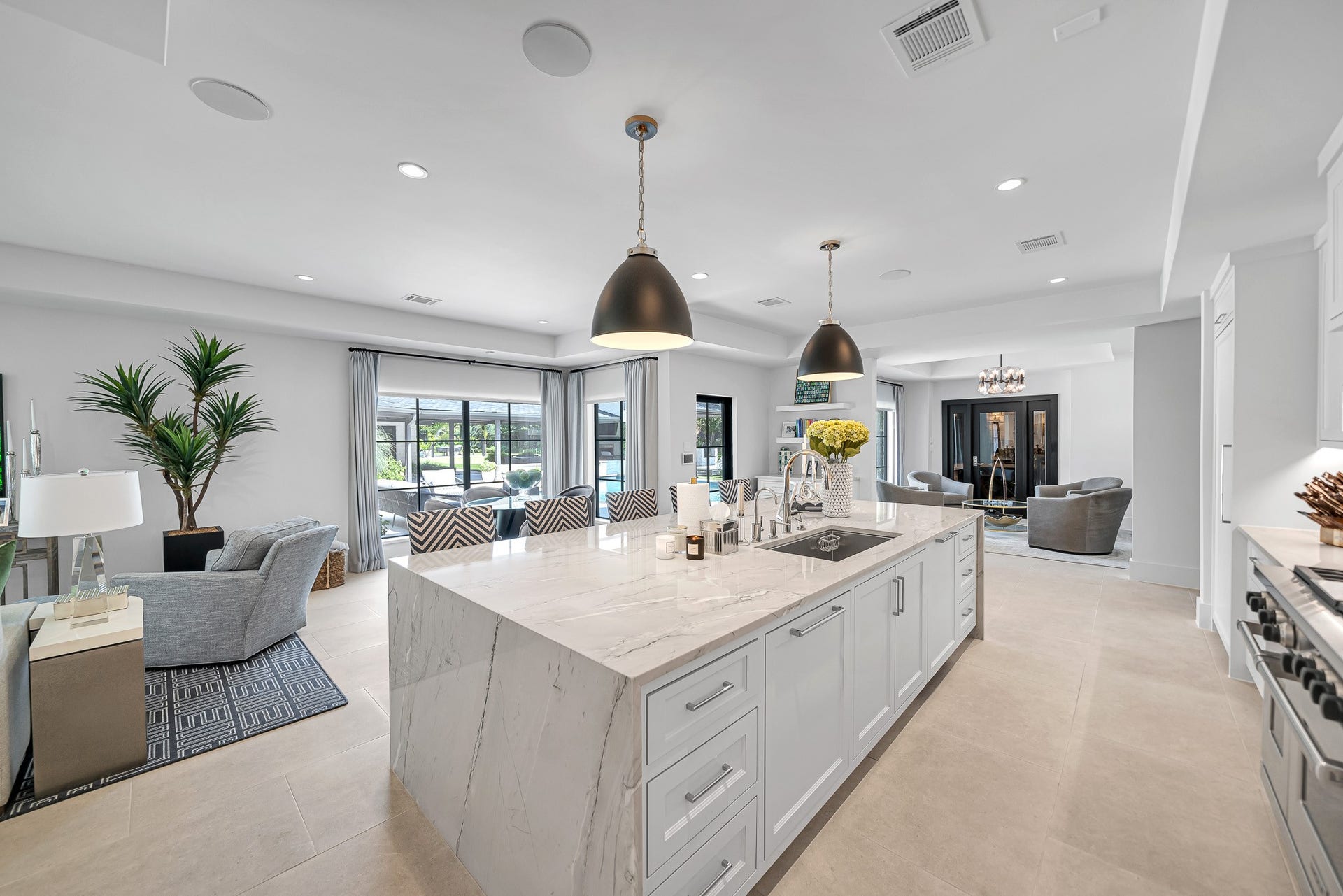 Oversized center island includes a built-in sink with hot/cold filter, sleek chrome hardware, lower storage drawers, and counter seating.