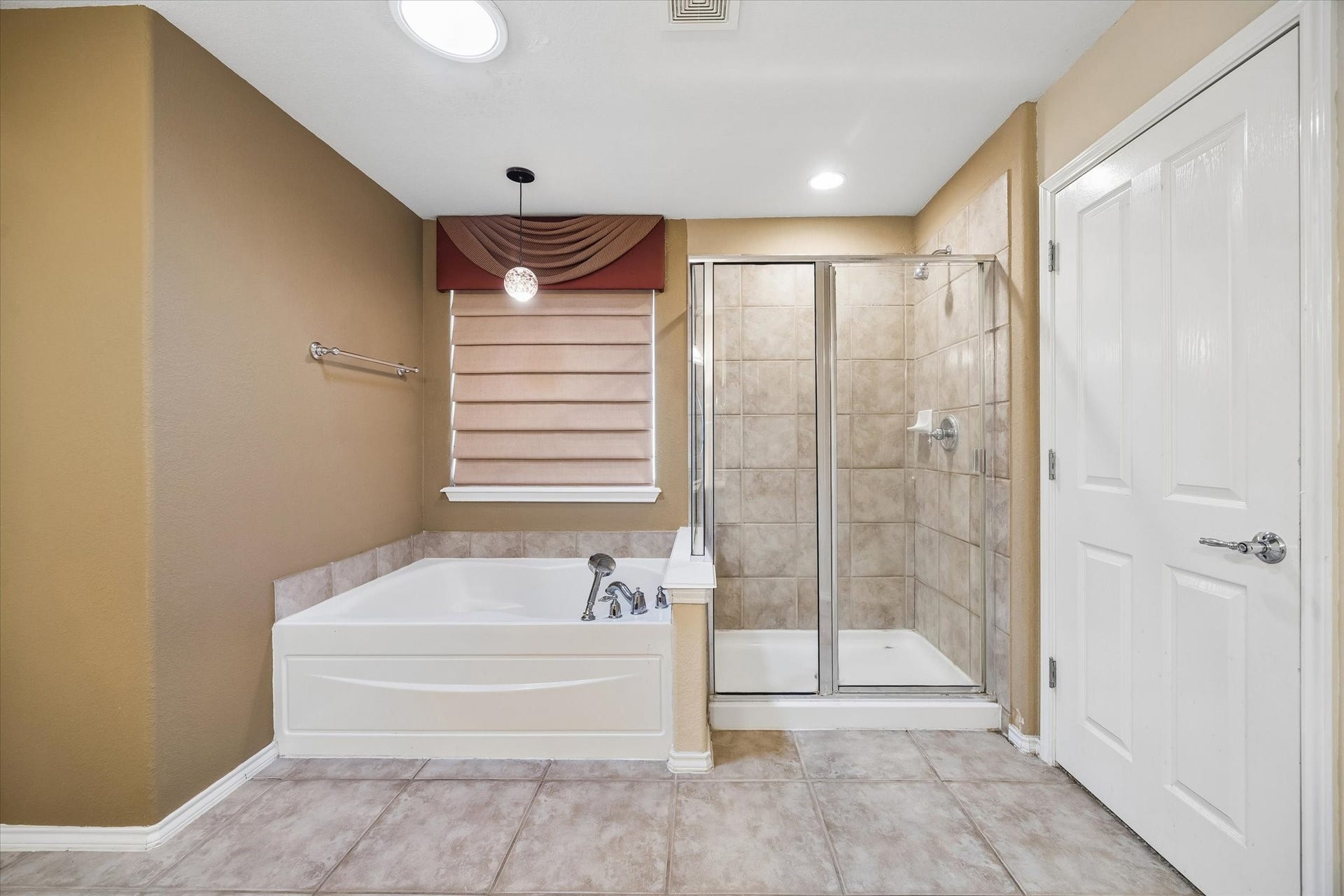 This spacious primary bathroom featuring a spacious bathtub and a separate glass-enclosed shower, dual sinks and neutral tones.