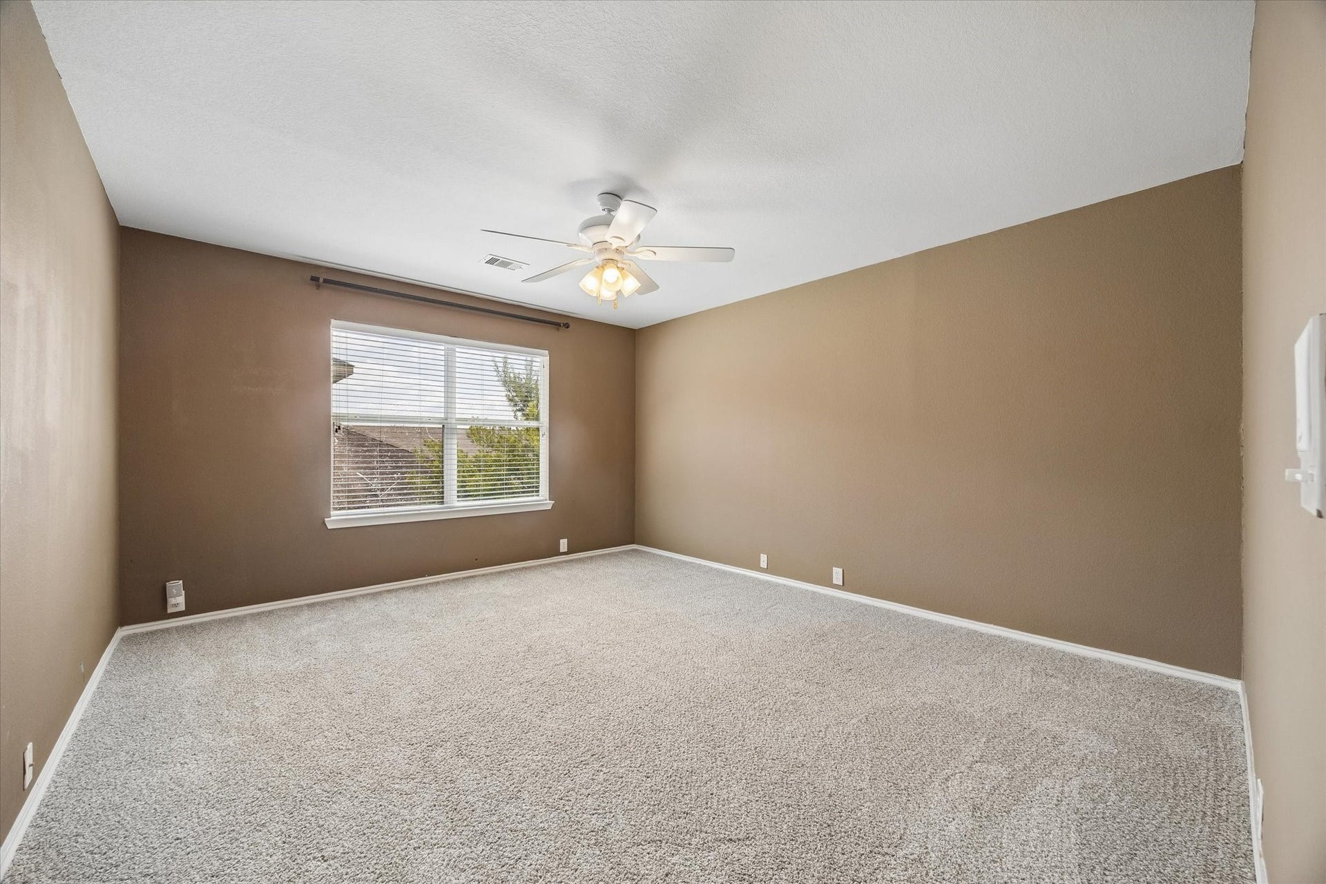 Spacious secondary bedroom featuring plush carpeting, neutral-toned walls, and abundant natural light from a large window, complete with an elegant ceiling fan for comfort and style.