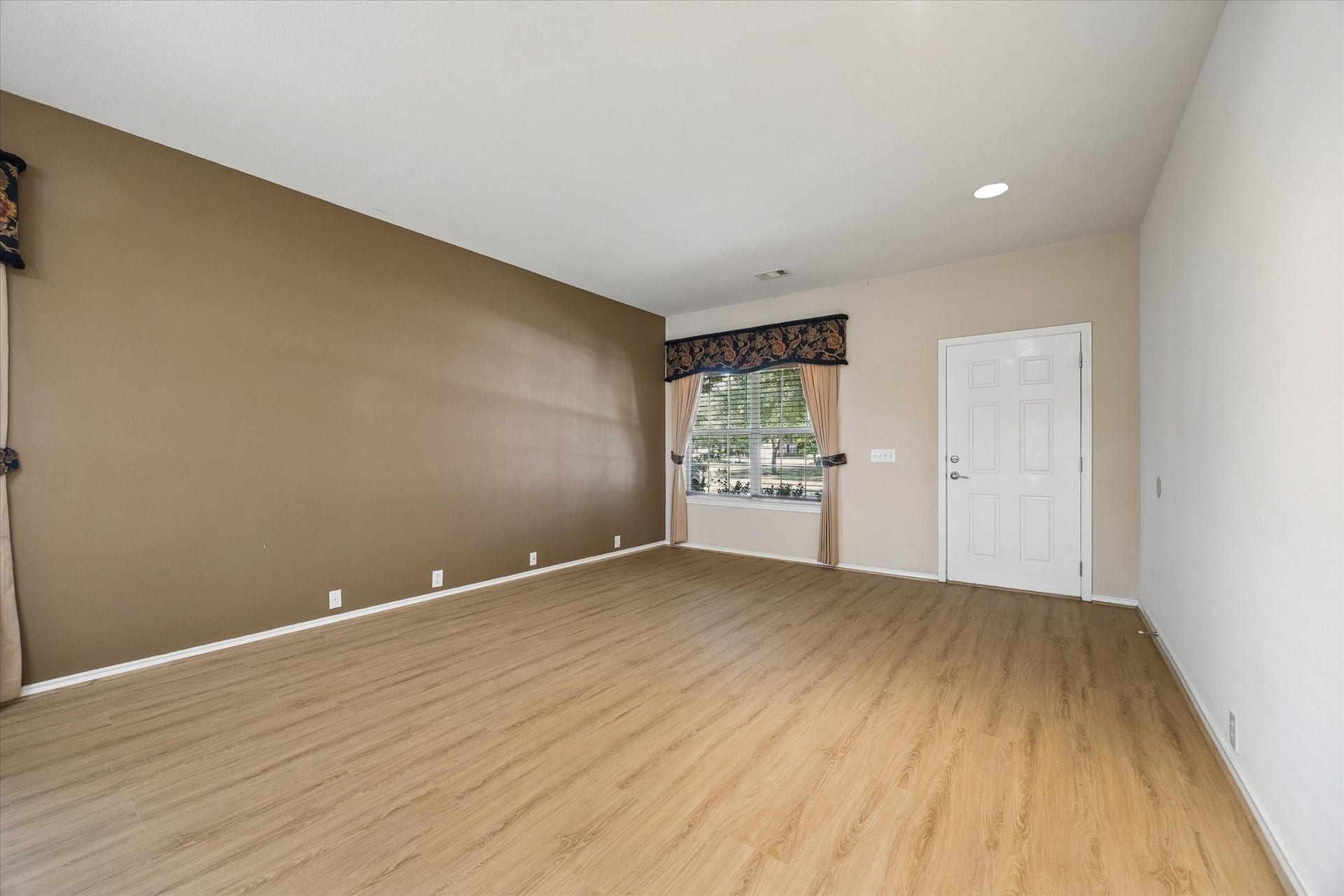 Spacious room with warm wood flooring, neutral walls, and a large window providing ample natural light.