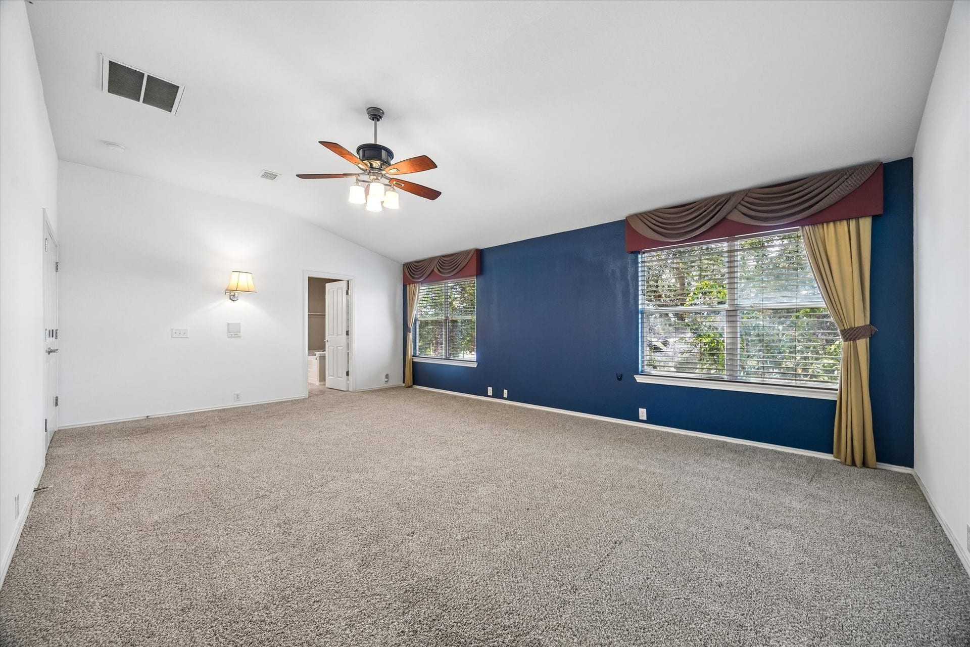 Spacious primary bedroom with plush carpeting, a striking blue accent wall, and large windows for natural light. A ceiling fan adds comfort to the room's charm.