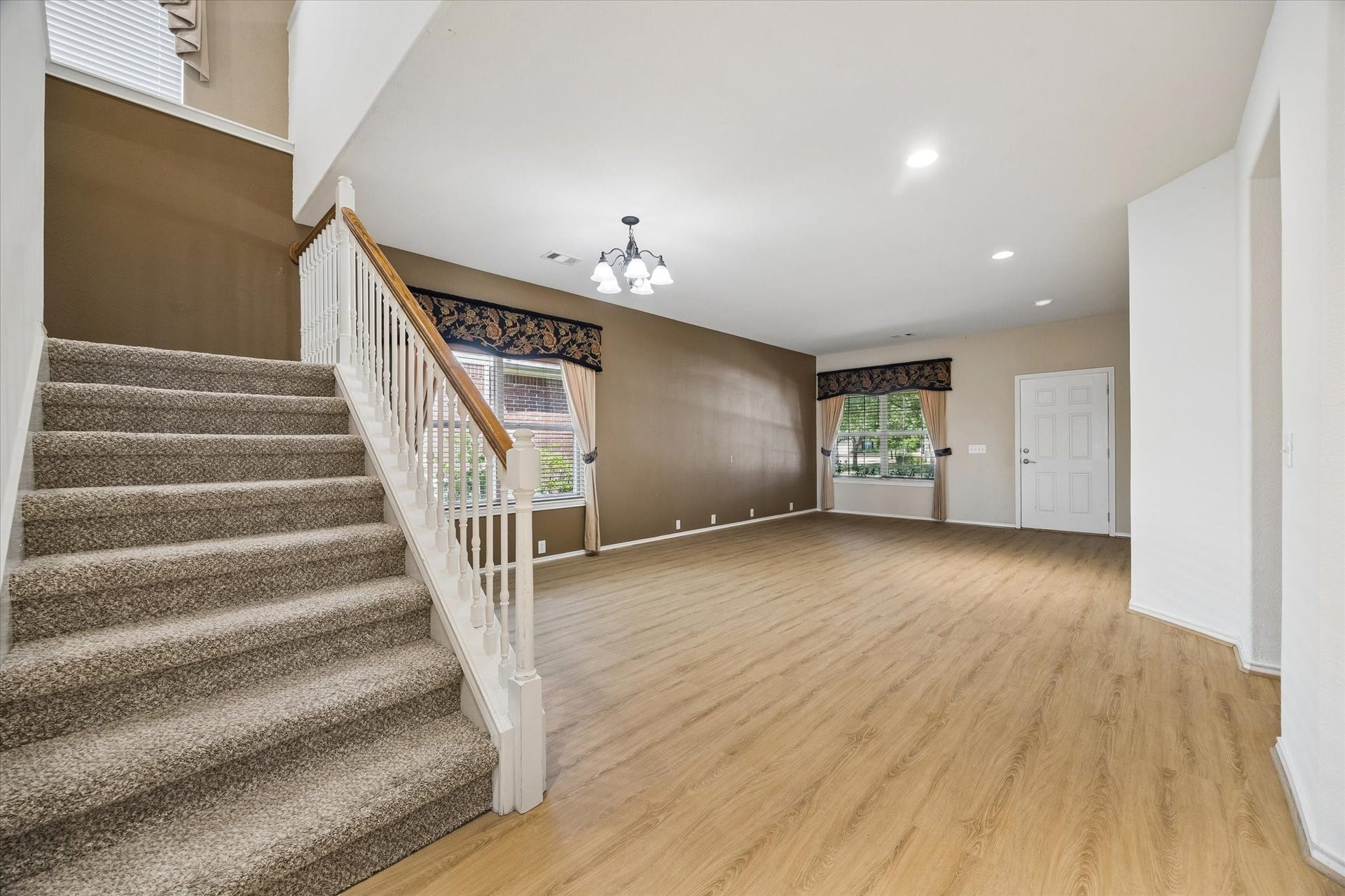 Spacious living area with elegant wood flooring, abundant natural light, and a welcoming staircase leading to the upper level.