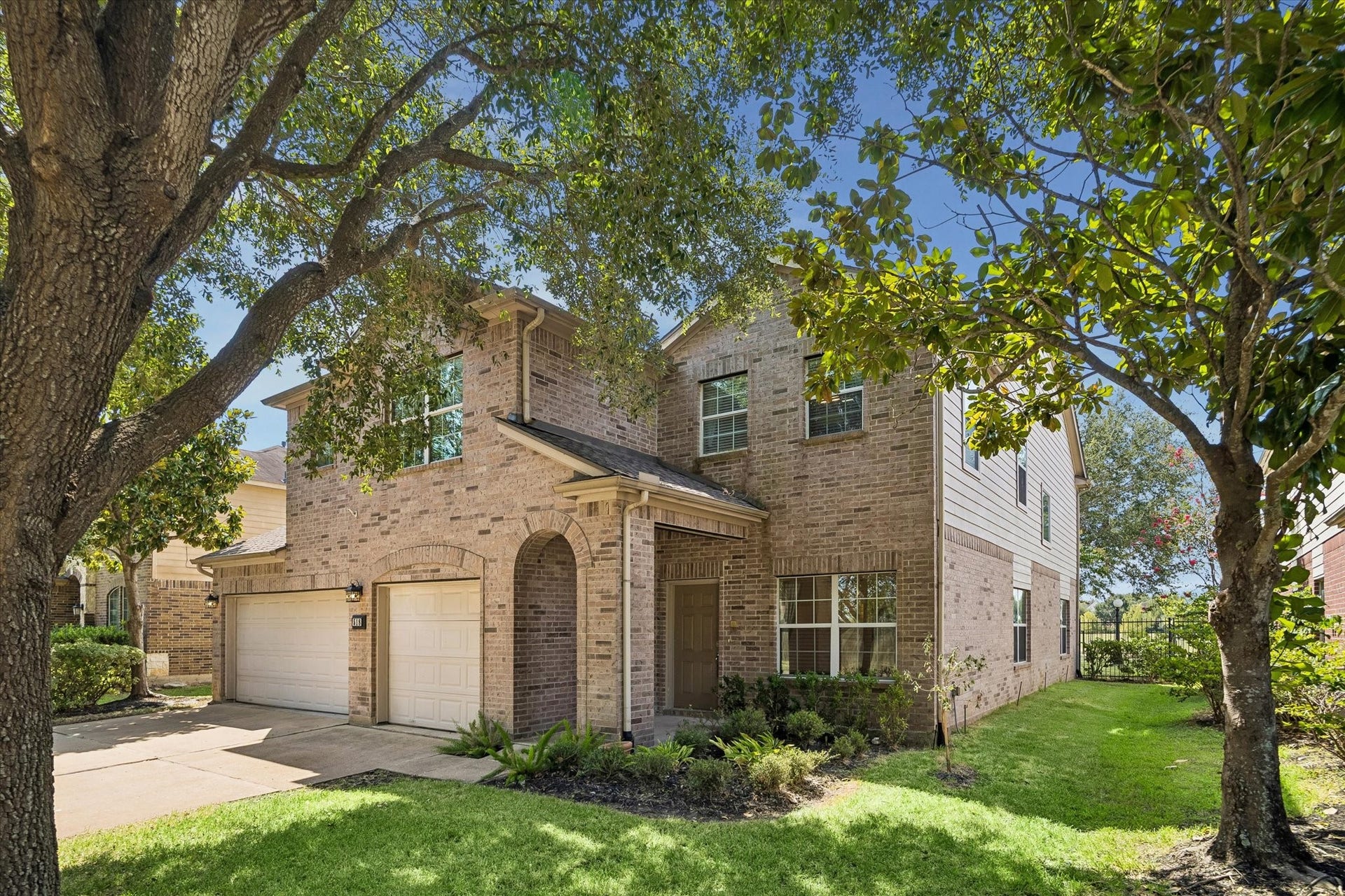 Charming two-story brick home with a three-car garage, nestled among mature trees and lush landscaping, offers inviting curb appeal.