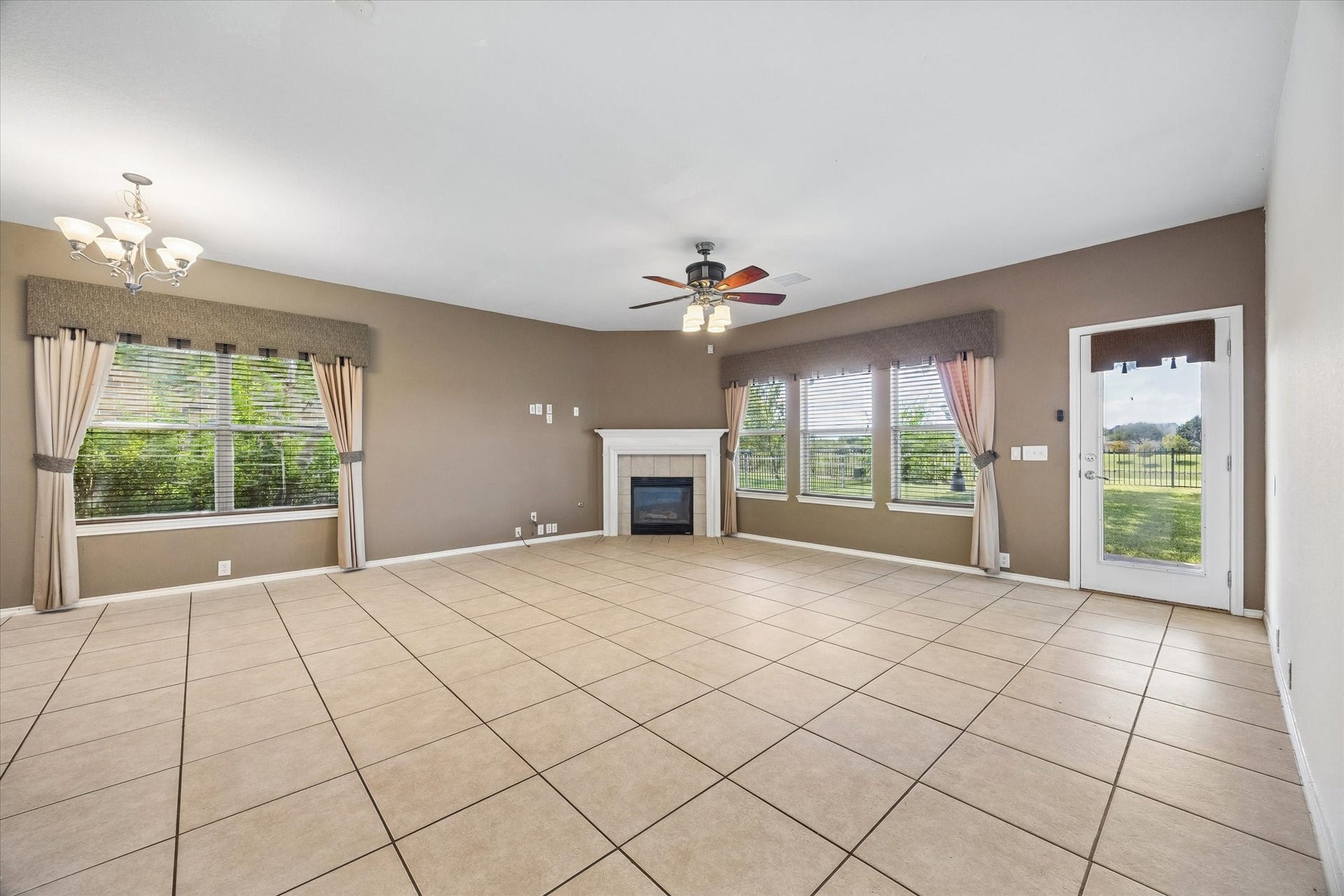 Spacious family room with large windows offering natural light, a cozy fireplace, elegant tile flooring, and direct access to a scenic water-view backyard.