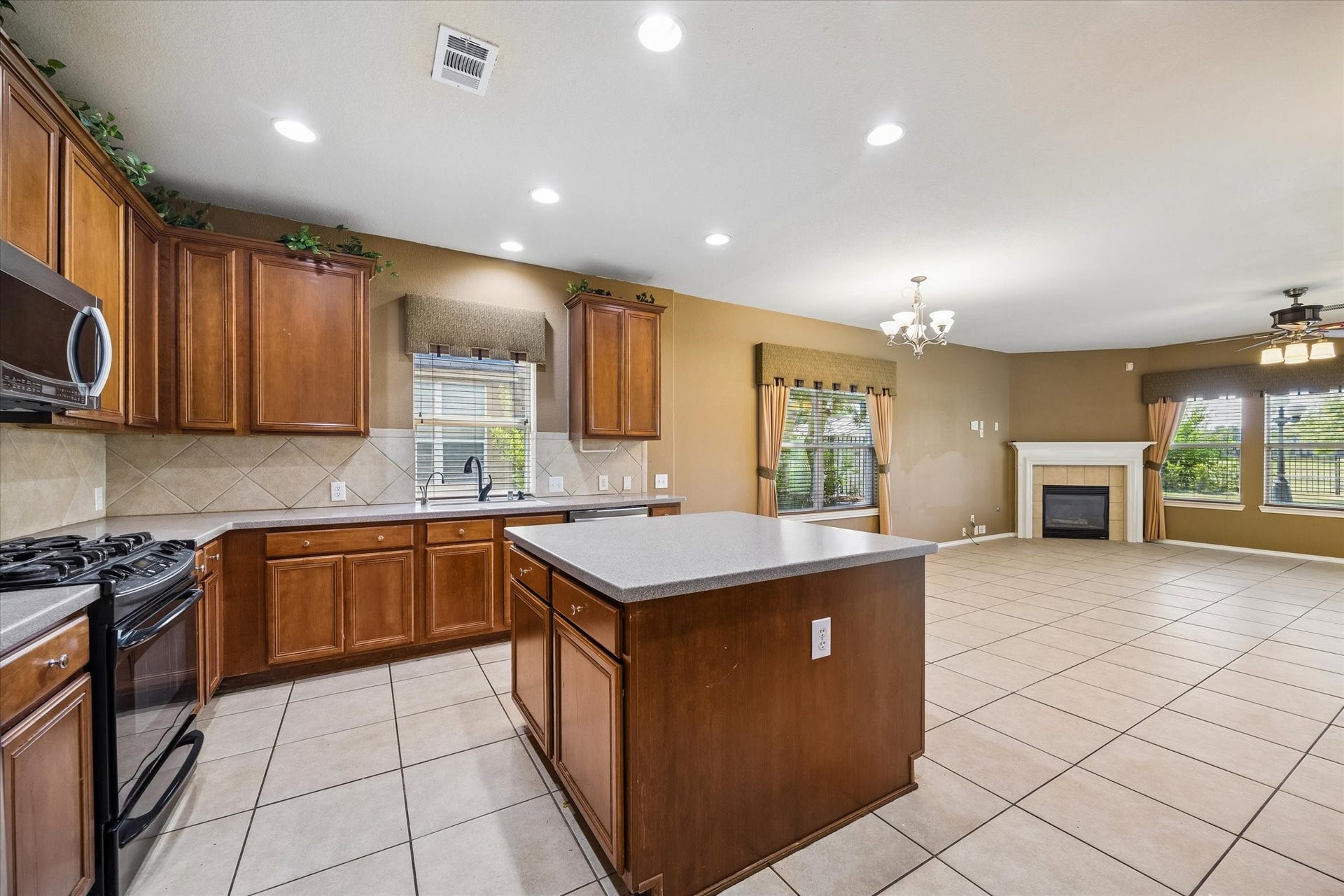 Spacious open-concept kitchen and living area featuring rich wooden cabinetry, a central island, and a cozy fireplace, all illuminated by ample natural light.