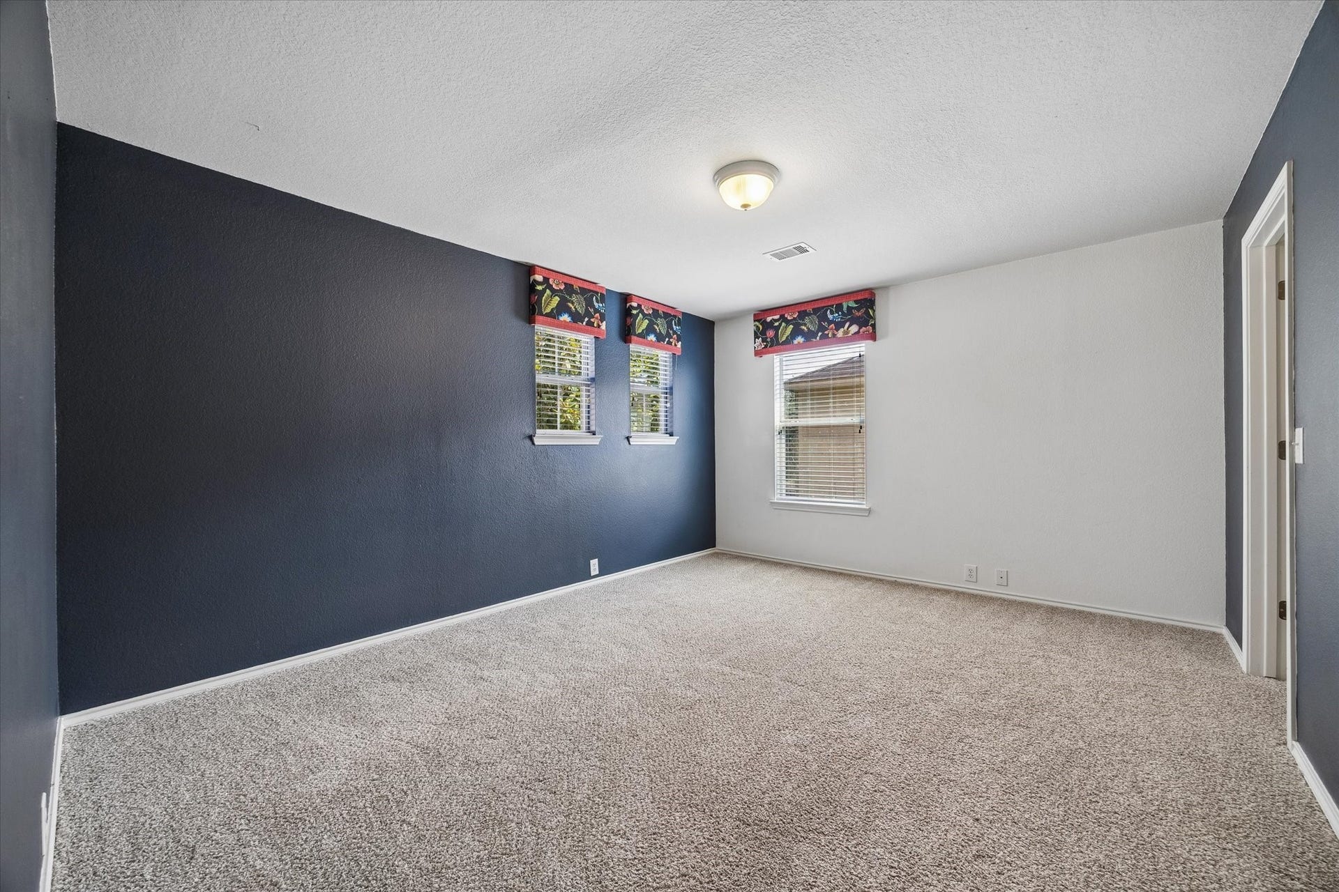 Spacious secondary bedroom with plush carpet and deep blue accent walls, featuring large windows that provide plenty of natural light and style.