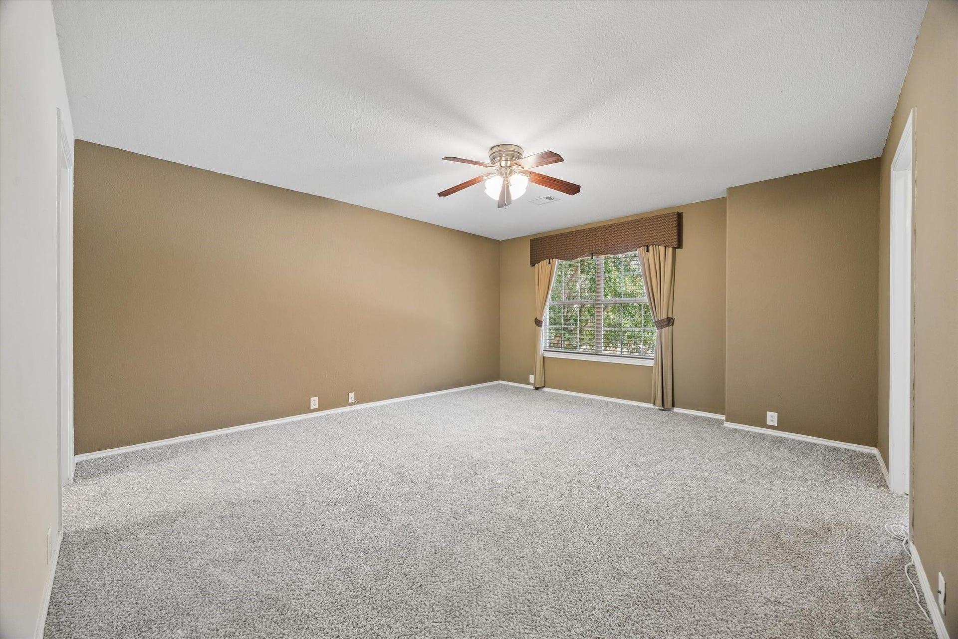 Spacious secondary bedroom with warm neutral walls, plush carpeting, and a ceiling fan, complemented by a large window.