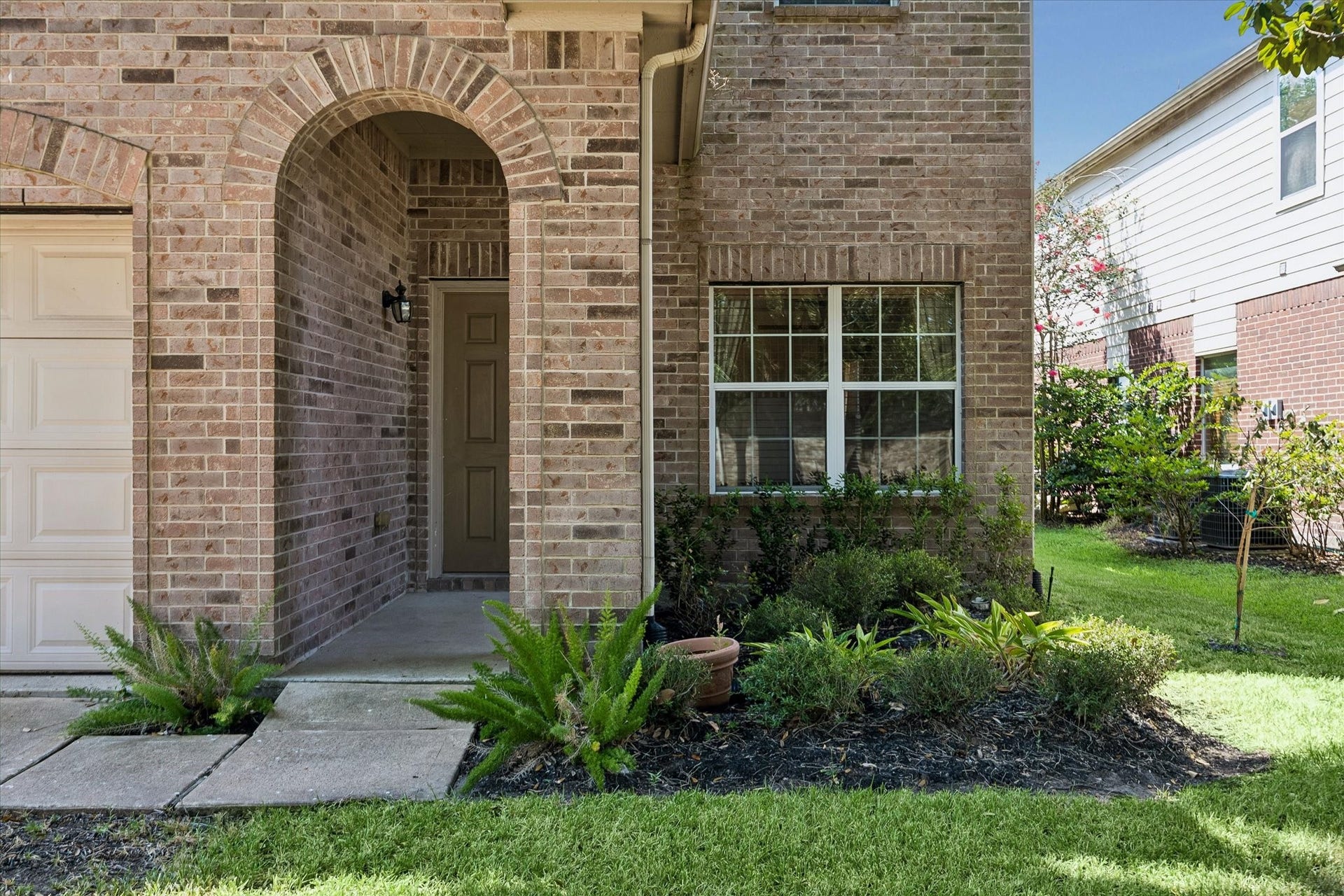 Charming brick exterior with an inviting archway and neatly landscaped yard offering a warm and welcoming entrance.