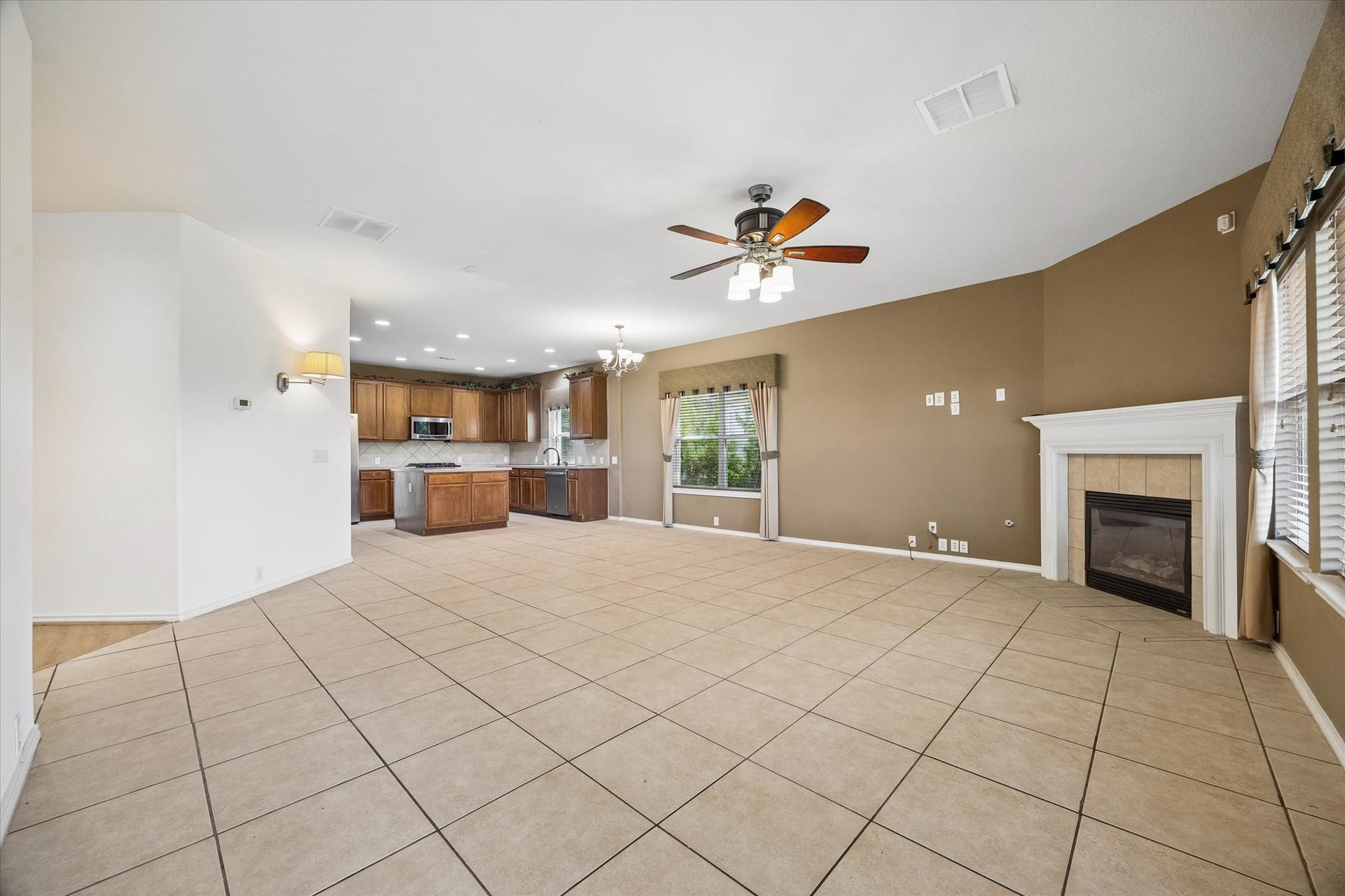 Spacious open-concept living area with a cozy fireplace, large windows, and tile flooring, seamlessly connecting to a modern kitchen with plenty of cabinetry.