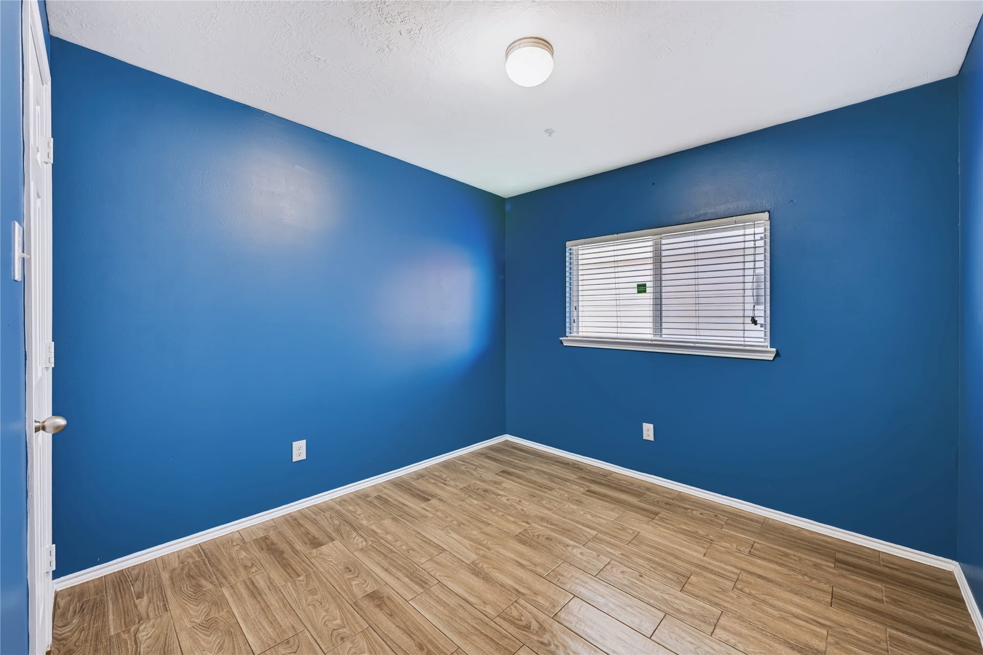 Bright and inviting secondary bedroom featuring rich wood-look tile flooring, a large window with natural light, and a flexible layout.
