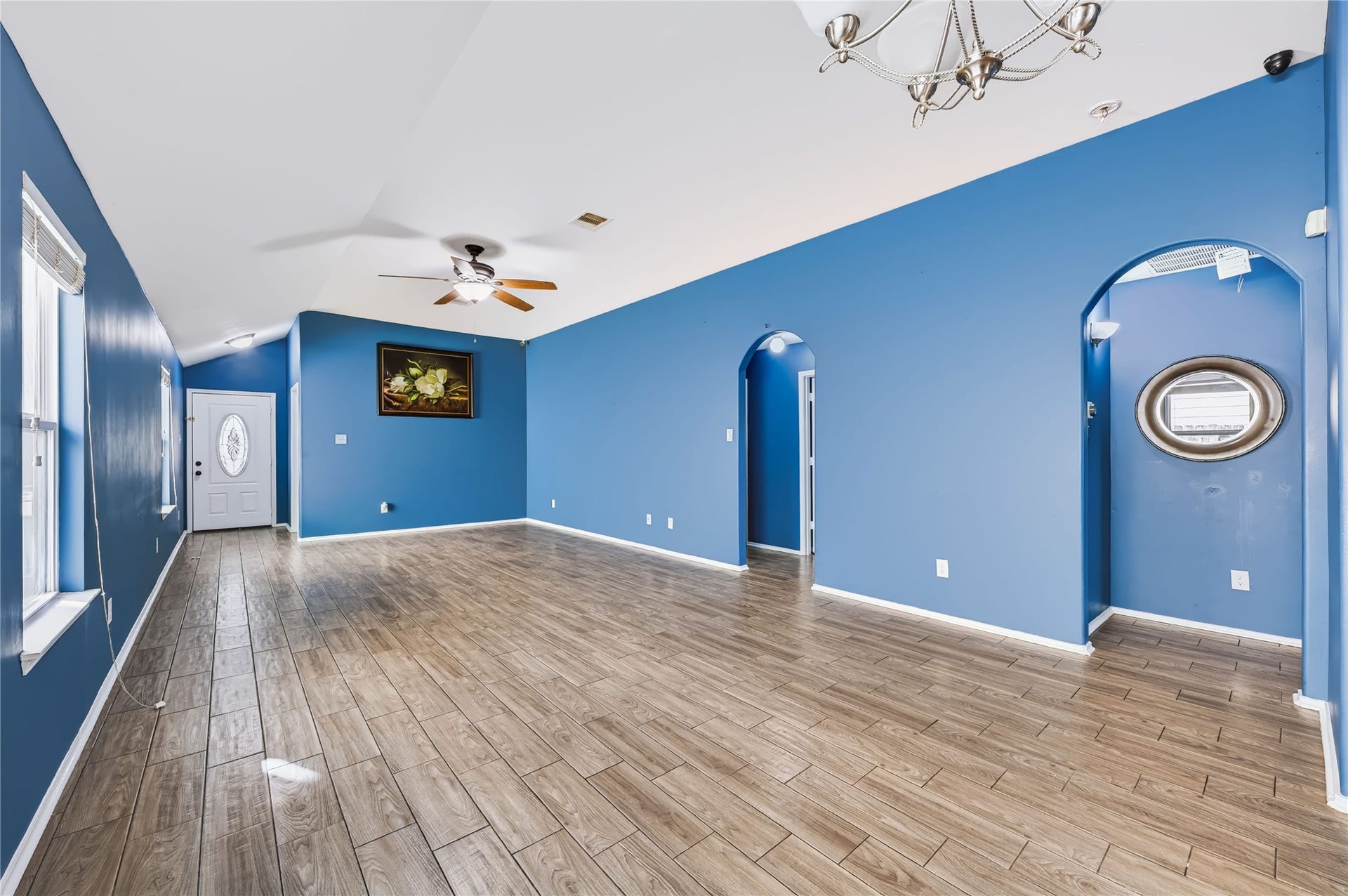 Spacious open-concept living area featuring rich wood-look tile flooring, vaulted ceilings, a modern ceiling fan, and vibrant accent walls.