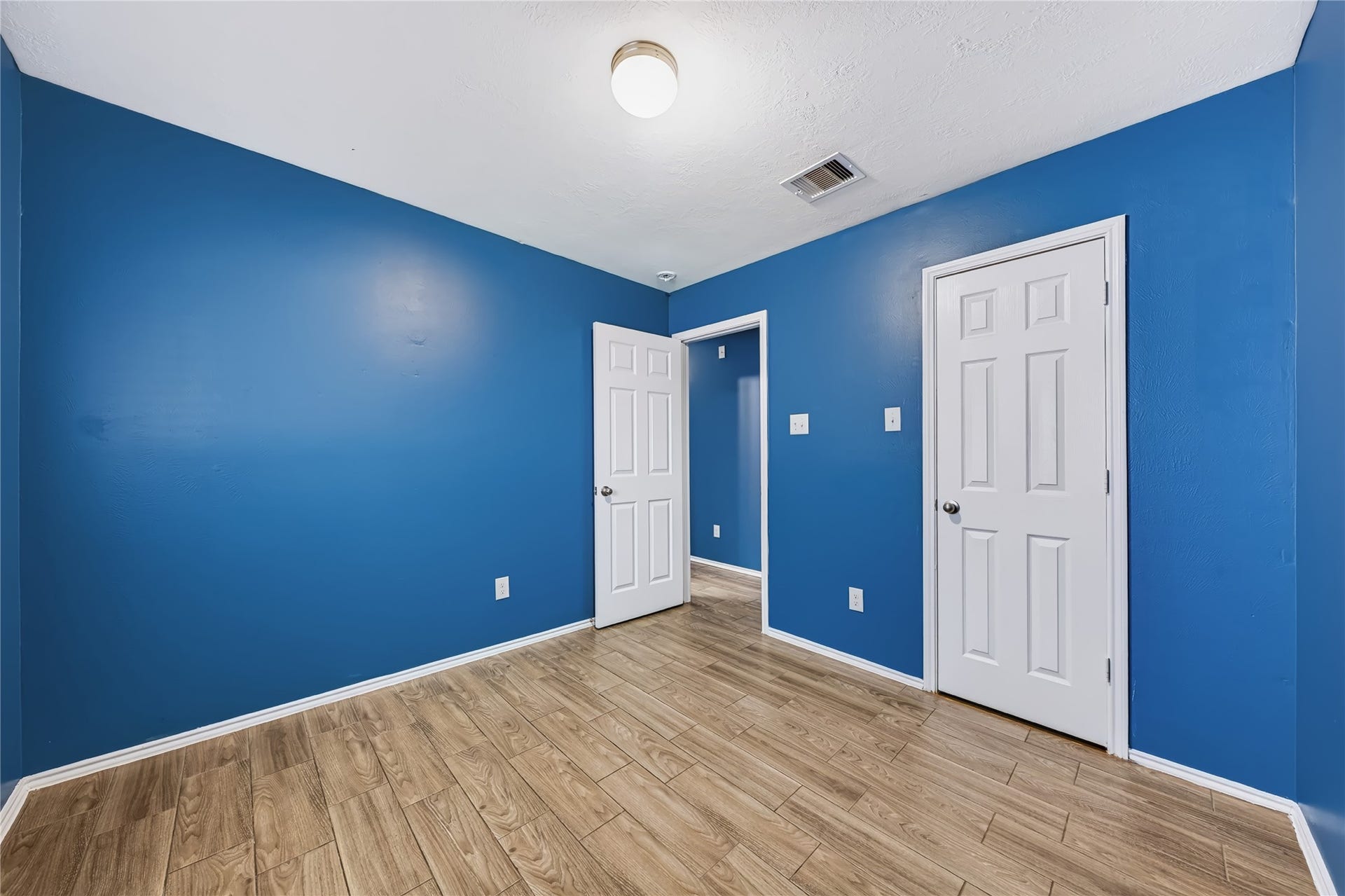 Bright and inviting secondary bedroom featuring rich wood-look tile flooring, a large window with natural light, and a flexible layout.