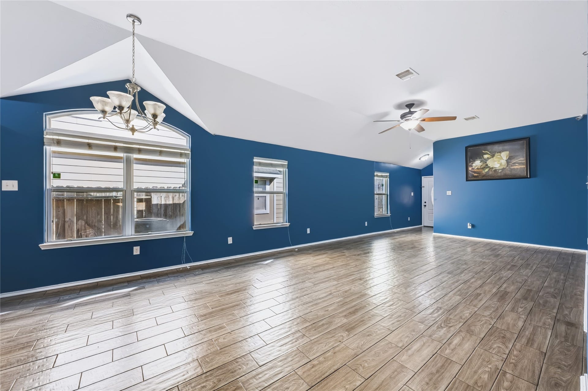 Spacious open-concept living area featuring rich wood-look tile flooring, vaulted ceilings, a modern ceiling fan, and vibrant accent walls.