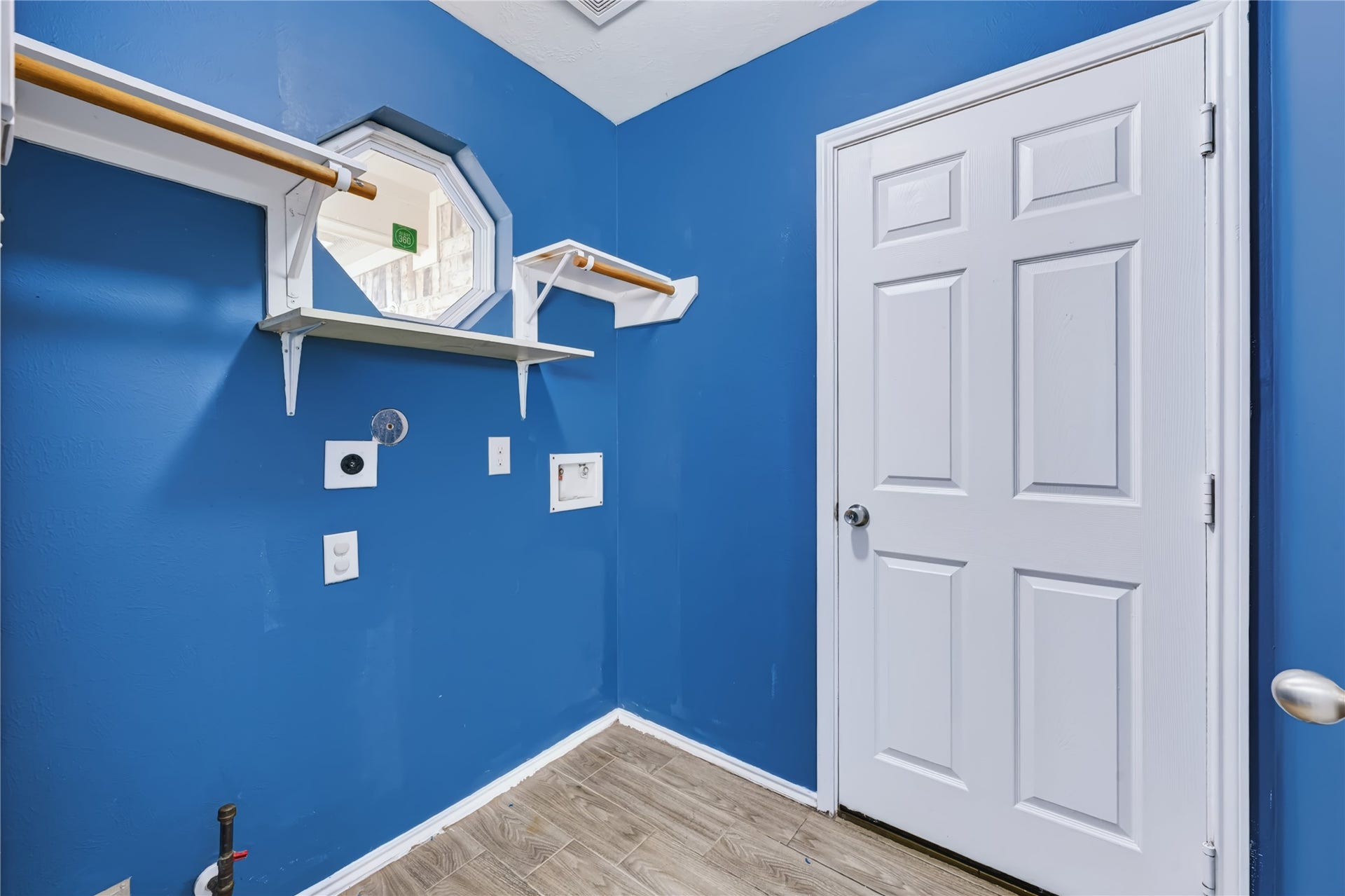 Convenient indoor utility room featuring washer and dryer connections, upper shelving for storage, and rich wood-look tile flooring.