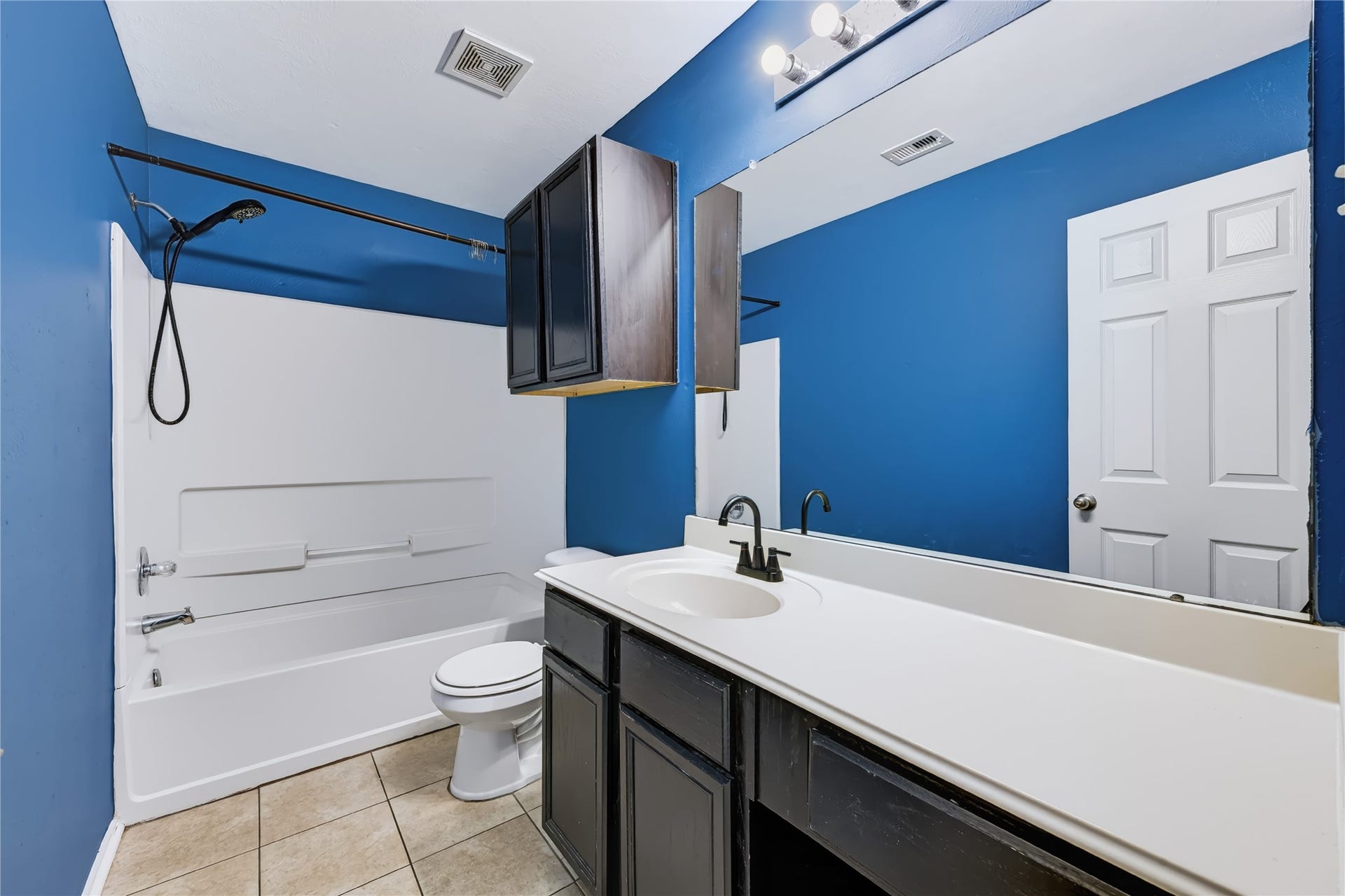 Bathroom featuring a tub/shower combination with a white surround, dark vanity cabinetry, a solid white countertop, and vibrant blue accent walls.