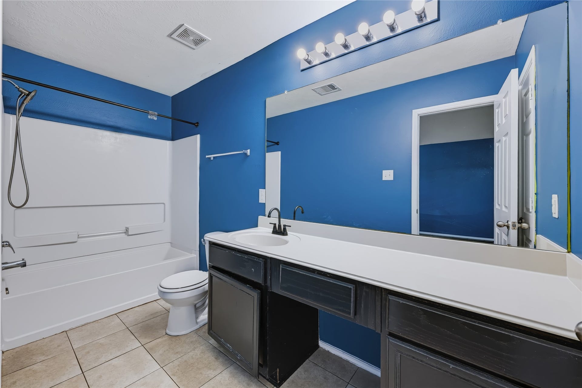 Well-appointed master bathroom featuring a spacious dual-sink vanity with dark cabinetry and solid white countertops, a large vanity mirror, and a tub/shower combination with a clean white surround