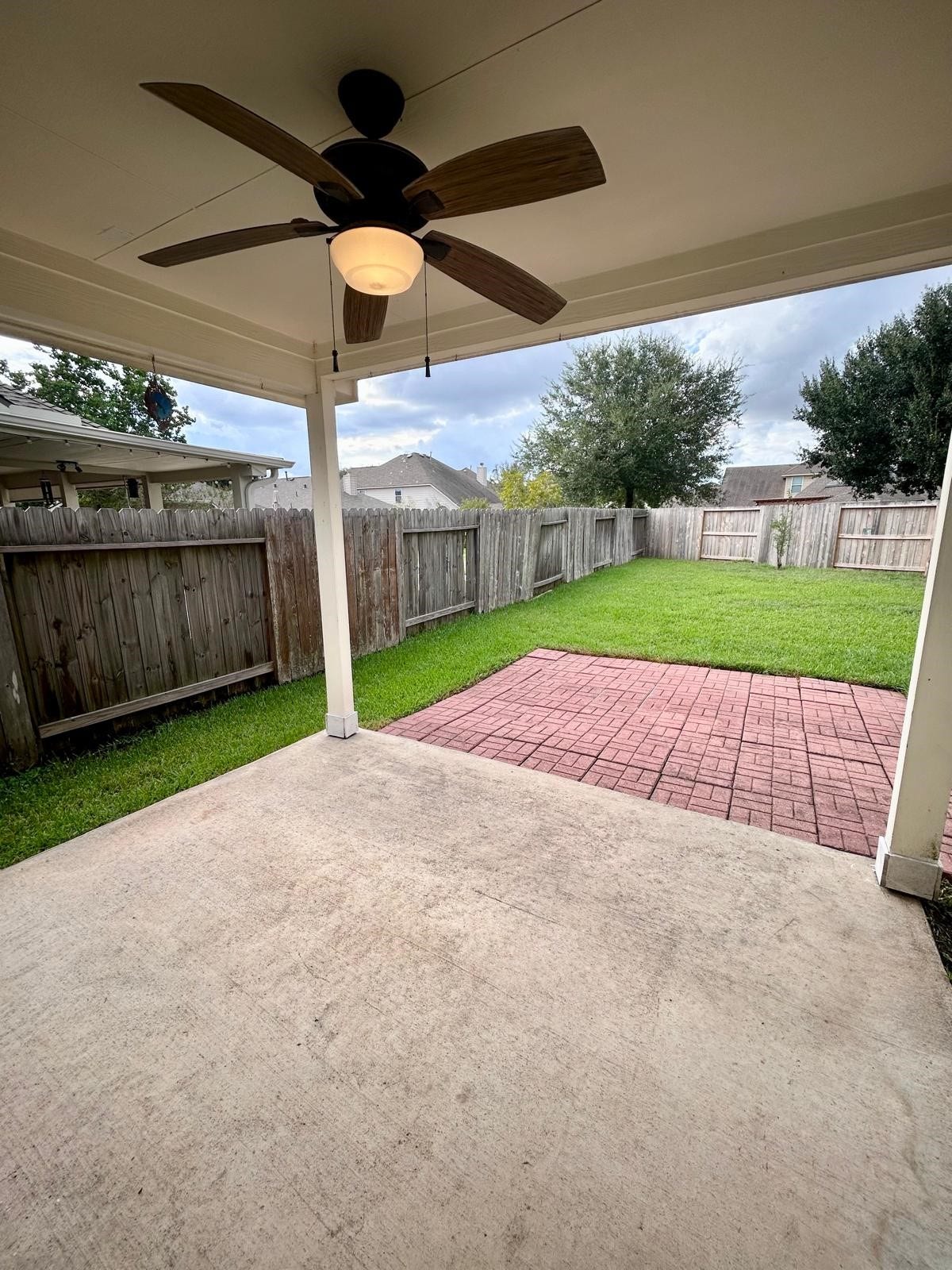 25918 Silver Timbers Lane, Katy, TX 77494 Covered patio with a ceiling fan overlooks a spacious backyard featuring a red brick patio and lush green lawn, perfect for outdoor relaxation and entertaining.