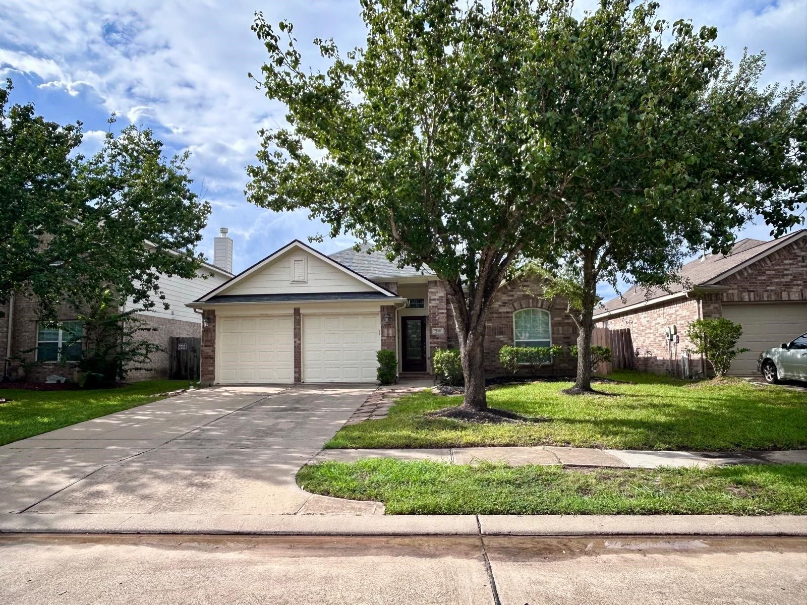 25918 Silver Timbers Lane, Katy, TX 77494 Charming single-story brick home with a spacious two-car garage, nestled among mature trees and lush greenery, offering a welcoming front yard.