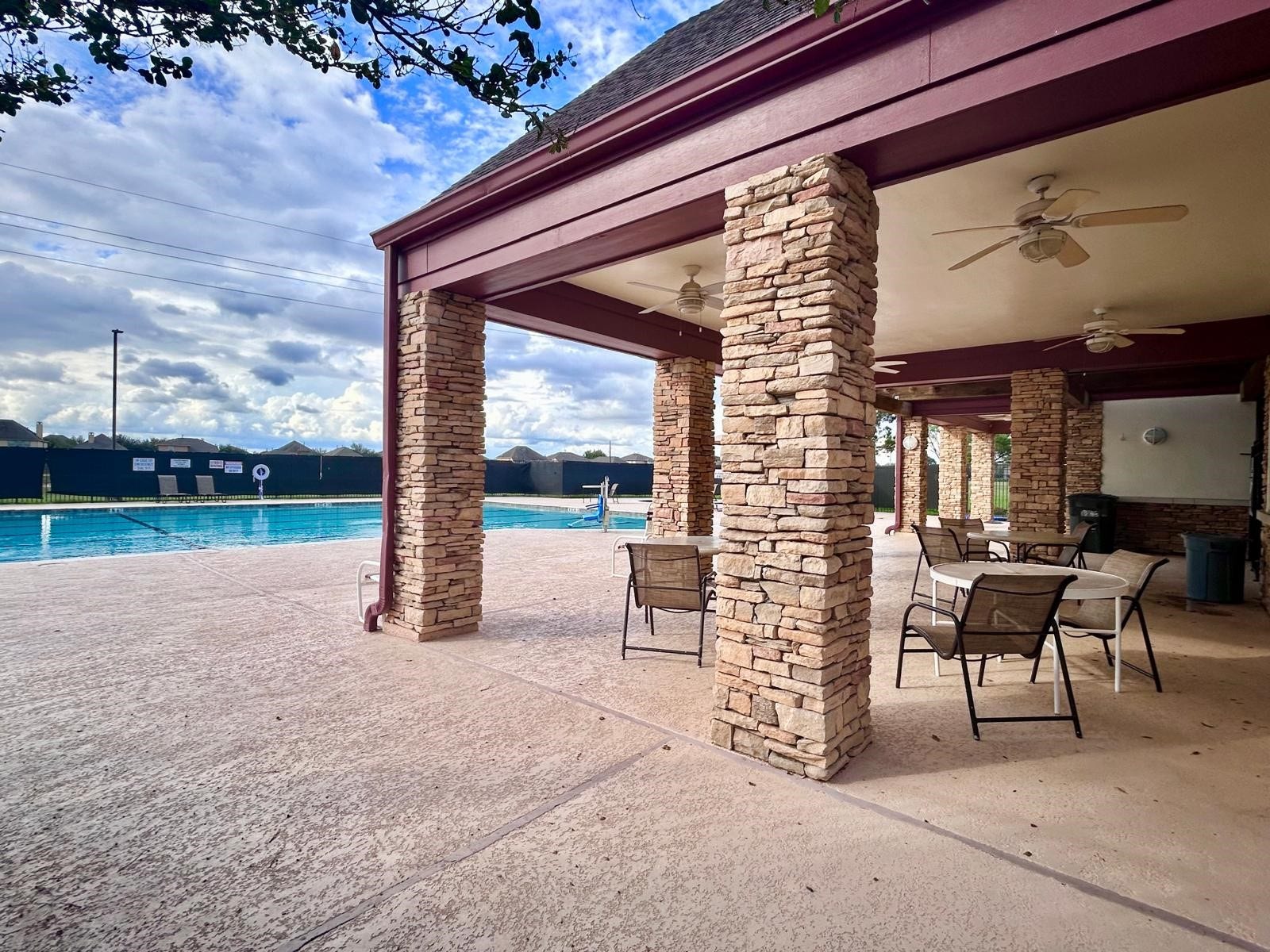 25918 Silver Timbers Lane, Katy, TX 77494 Spacious outdoor patio with stone columns, ceiling fans, and seating areas, overlooking a large, inviting pool perfect for relaxation and entertainment.