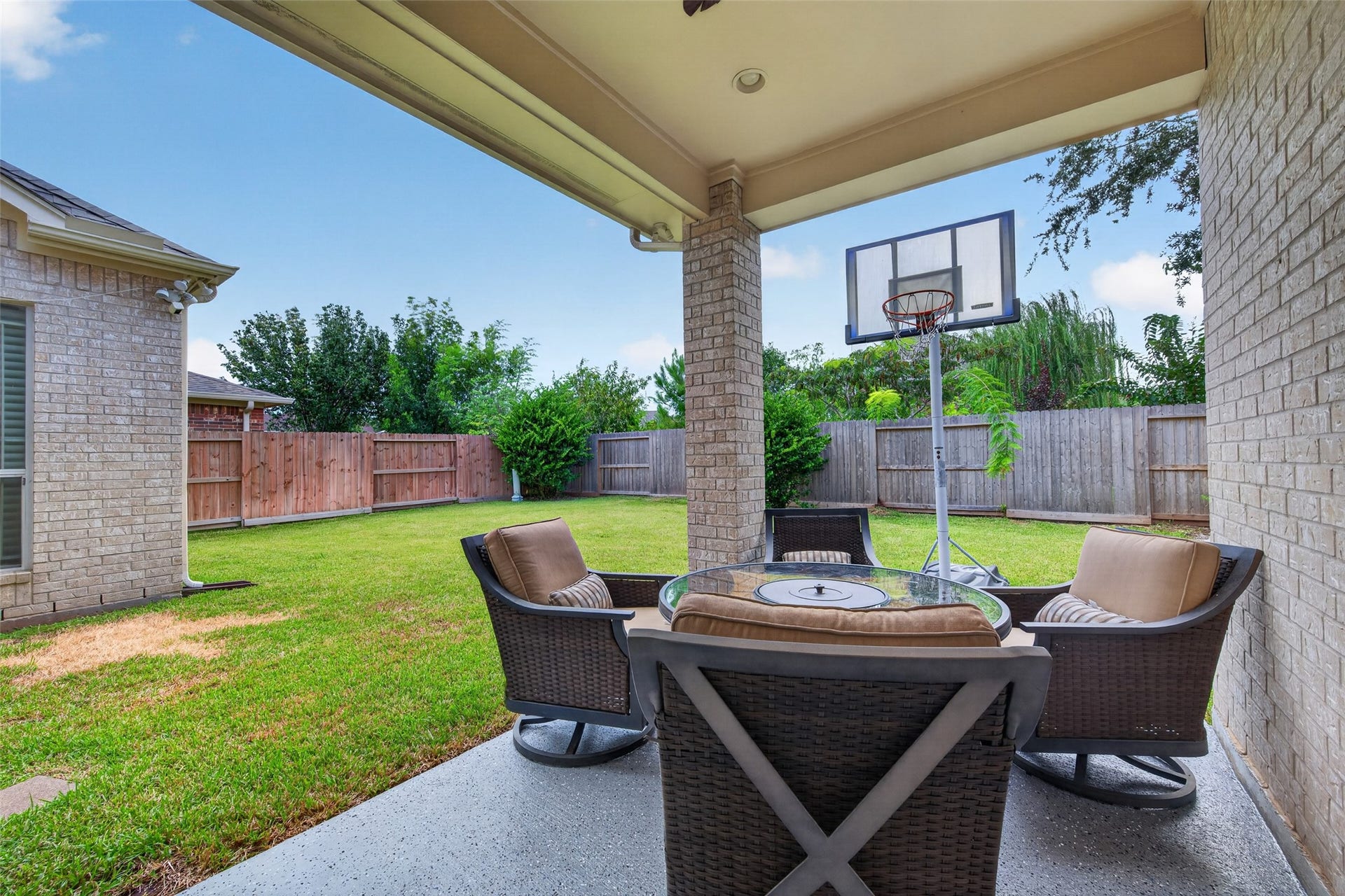 1814 Bartrum Street, Sugar Land, TX 77479 Charming covered patio with cozy seating and a basketball hoop, overlooking a spacious fenced backyard perfect for outdoor activities.