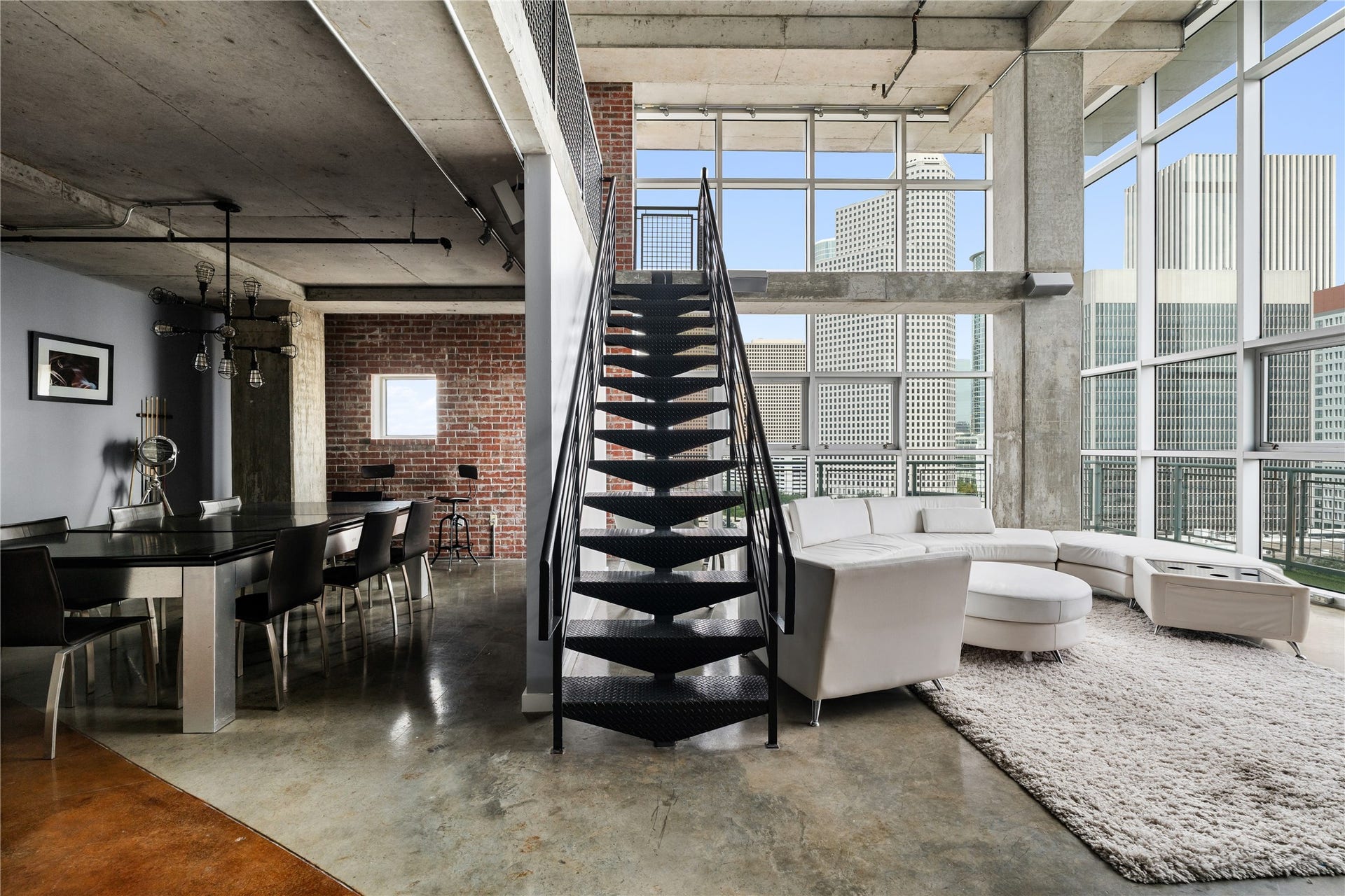A dramatic open staircase connects both levels while allowing the dining and living spaces to remain visually connected, showcasing the scale and openness of the loft.