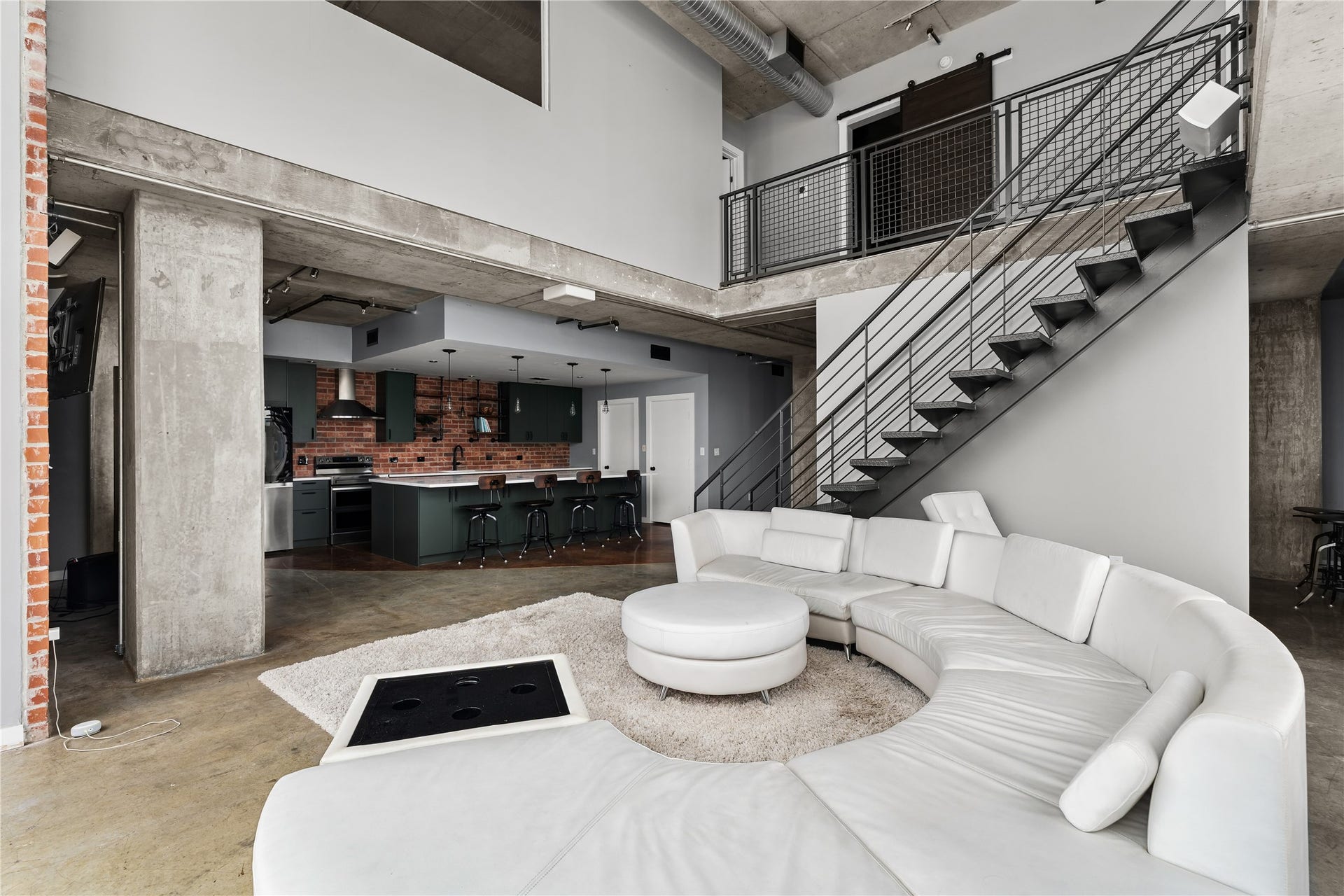 The main living area offers a more intimate setting within the lofts dramatic scale, framed by exposed concrete, the open staircase and a seamless connection back to the renovated kitchen.
